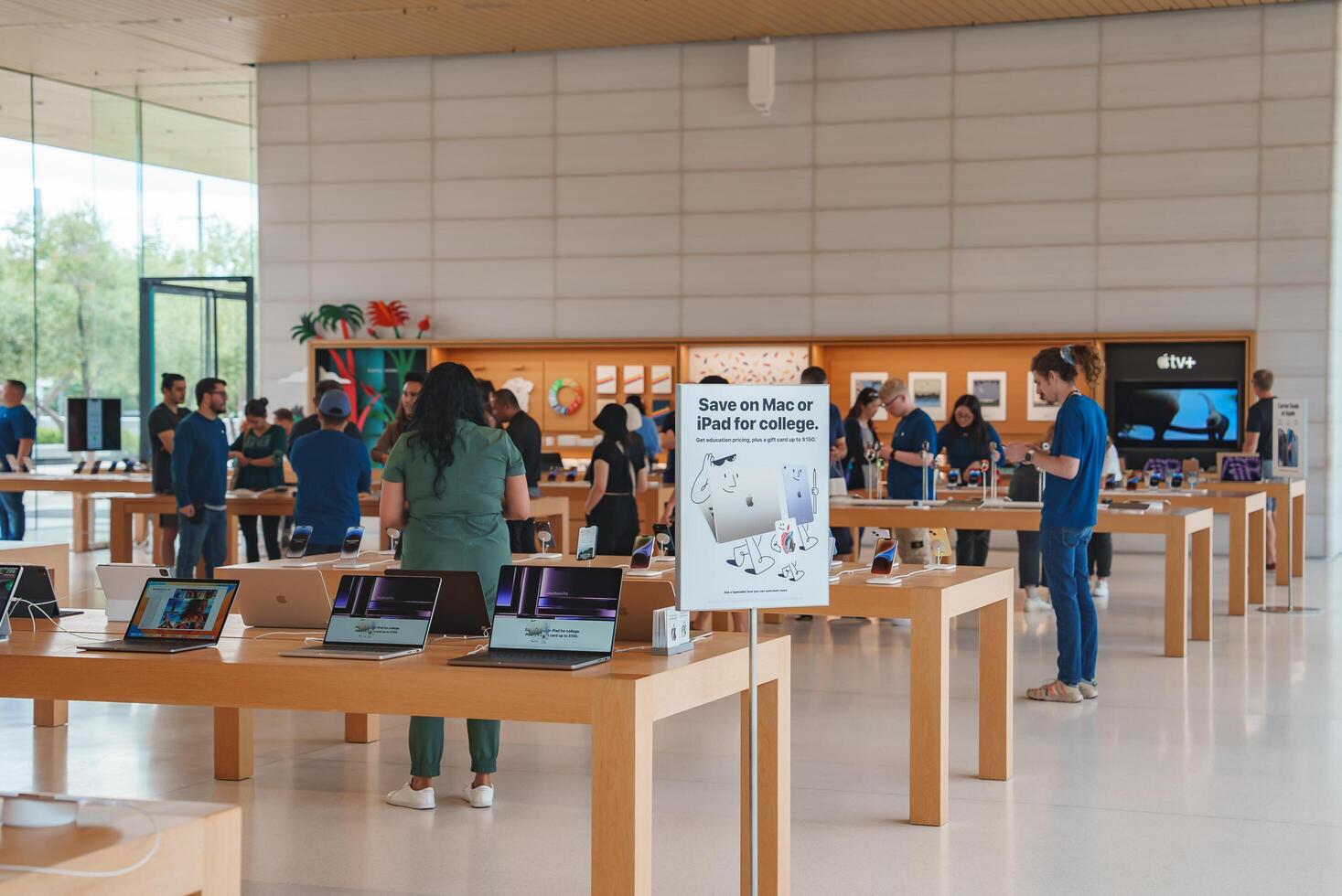 Modern and minimalistic Apple Store interior in Mountain View. Customers explore MacBooks, iPads, get help from employees. Bright, airy ambiance with wooden tables and promotional displays. photo