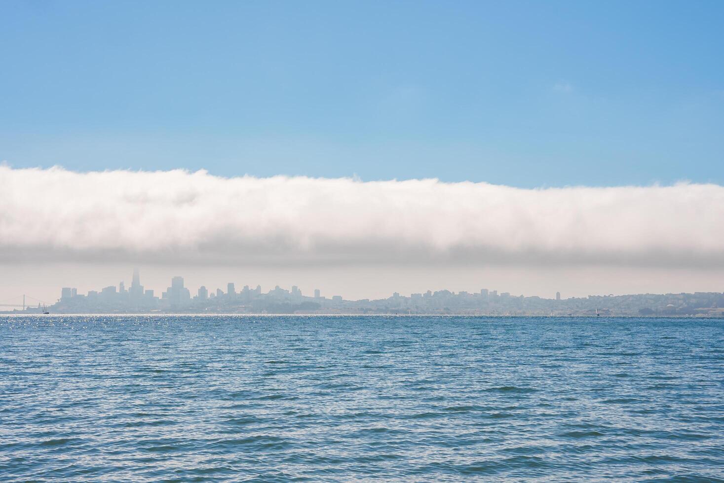 Discover the serene San Francisco skyline shrouded in low lying clouds, reflected in calm waters, under a clear sky. Iconic landmarks await in this picturesque cityscape. photo