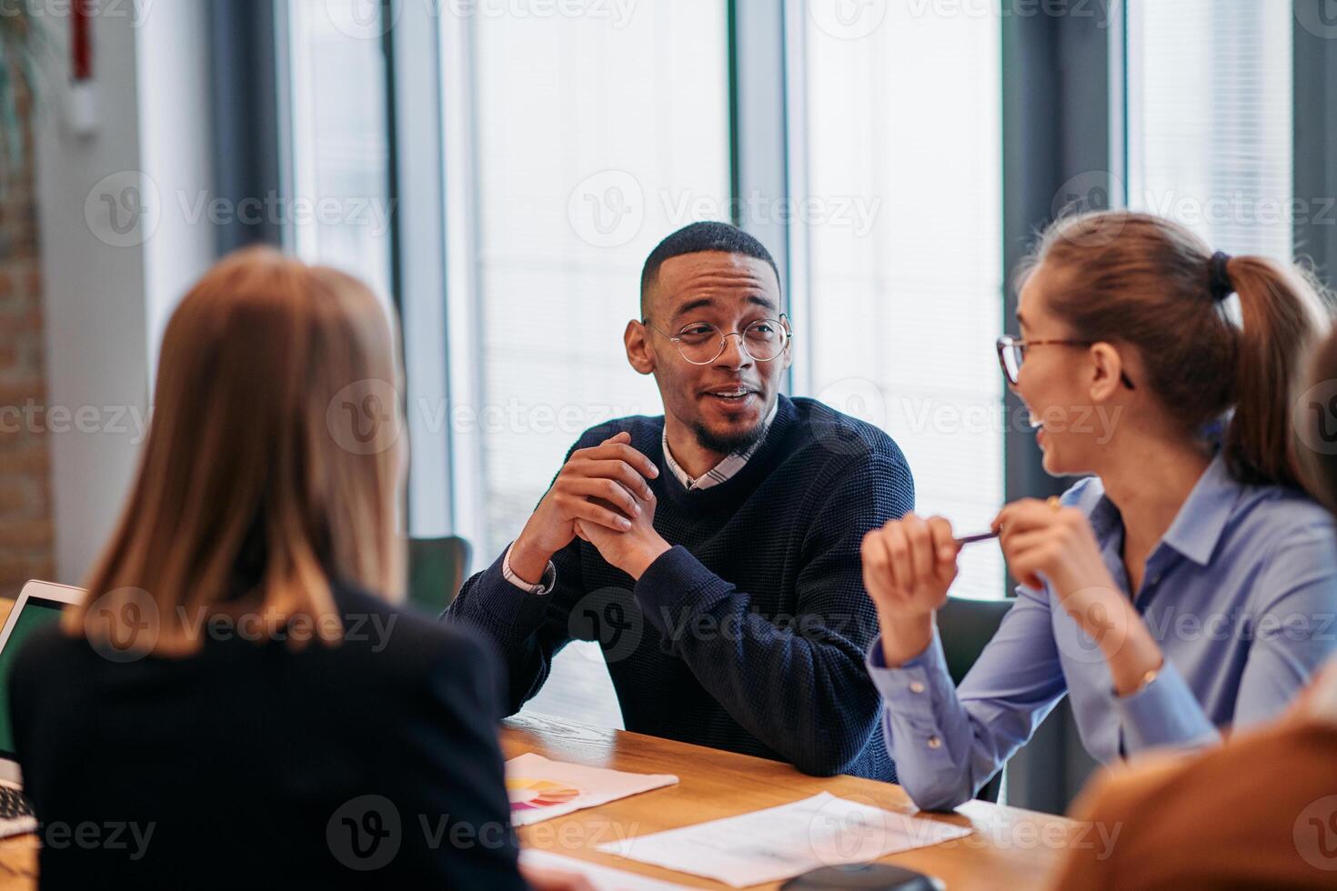 In the vibrant ambiance of a modern startup office, a diverse team of business professionals engage in discussions on various projects and develop new business strategies, epitomizing creativity and photo