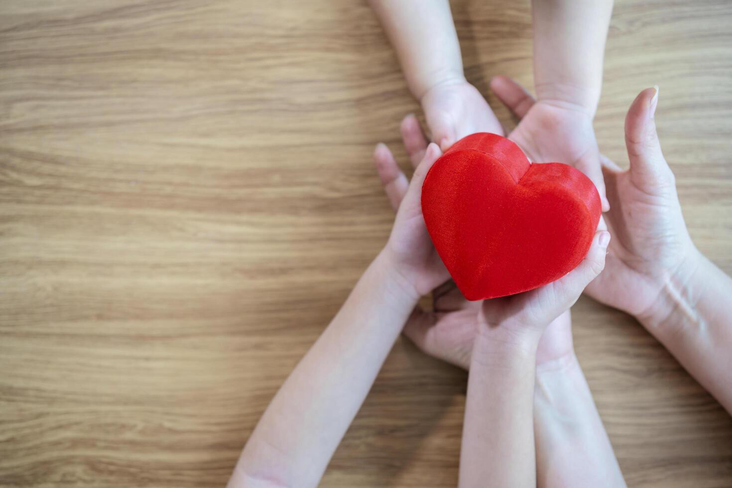red heart in child and mother hands on wooden background. concept of love, charity, empathy photo