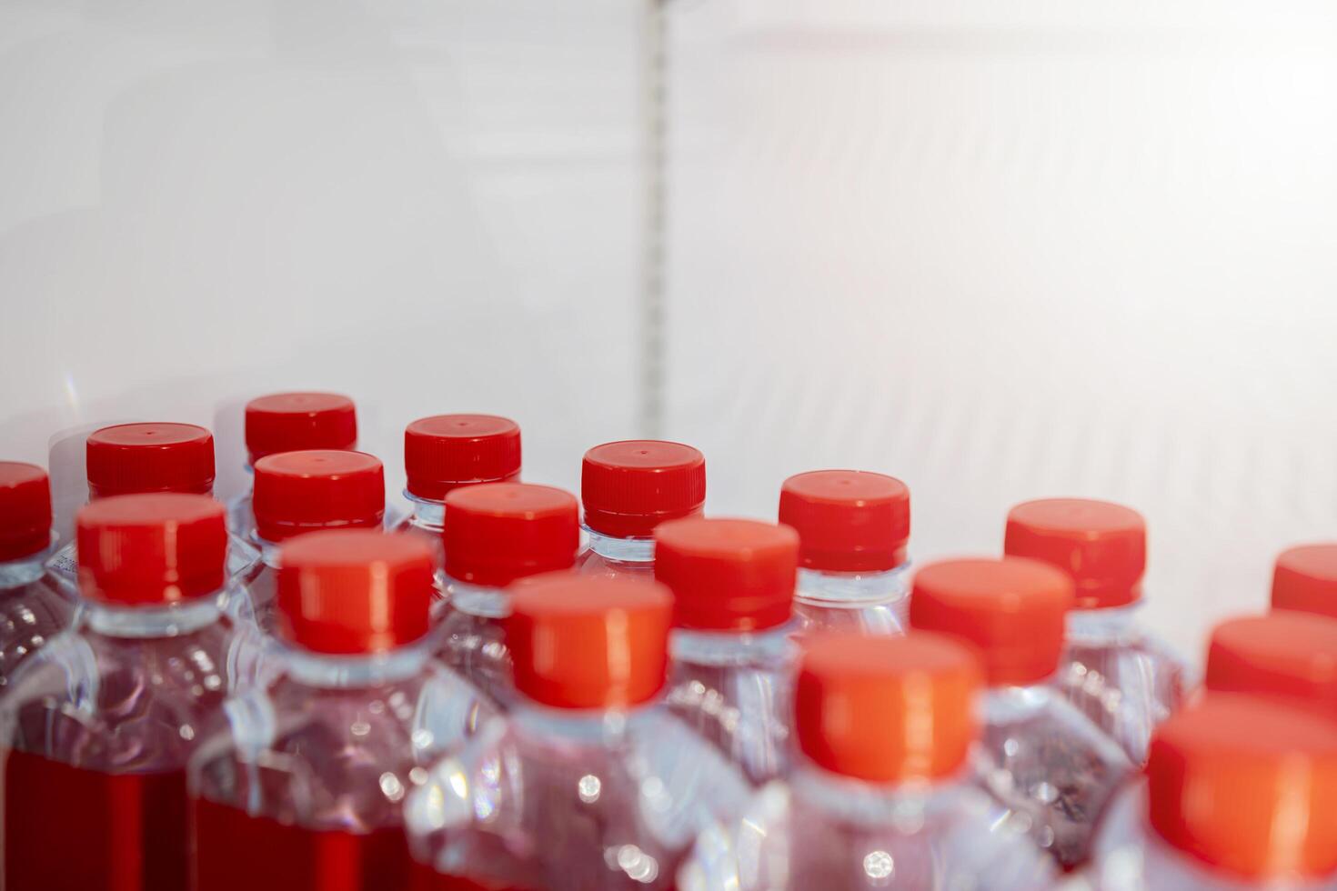 Rows of many transparent plastic bottles with drinking water supply in white refrigerator. Mineral water stack storage in fridge to drink on hot summer day. Bottle cap and red label photo