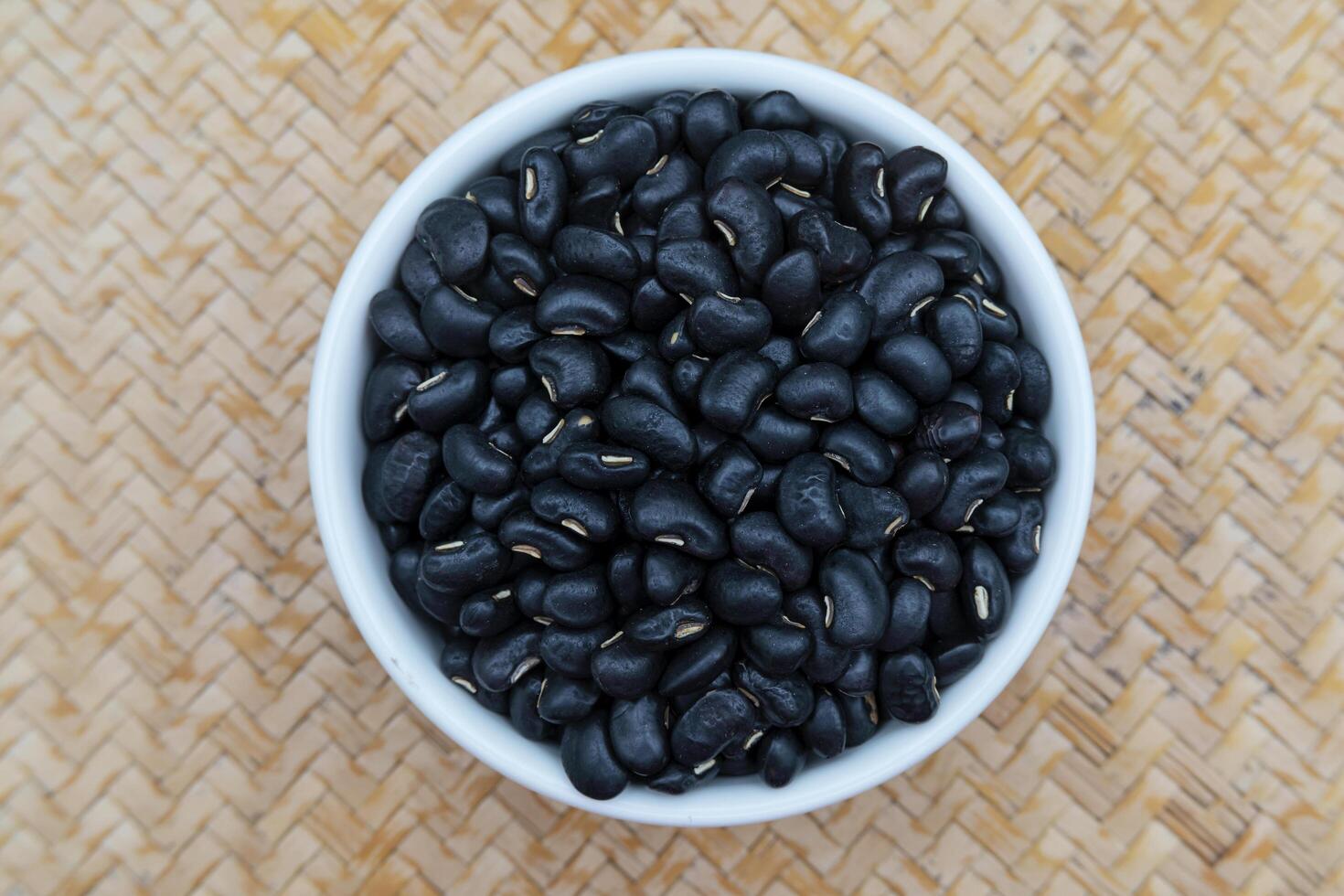 Black beans in a white ceramic bowl, placed on a wooden tray. photo