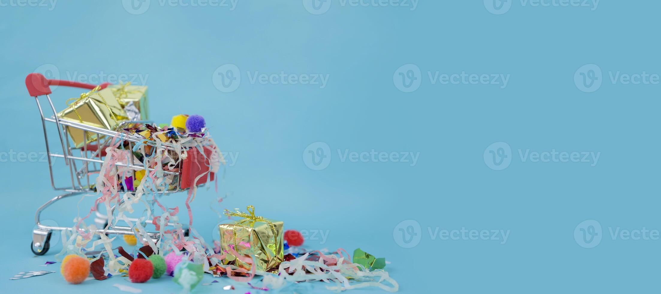 Supermarket cart placed on a blue background. There are gift boxes and colorful ribbons. photo