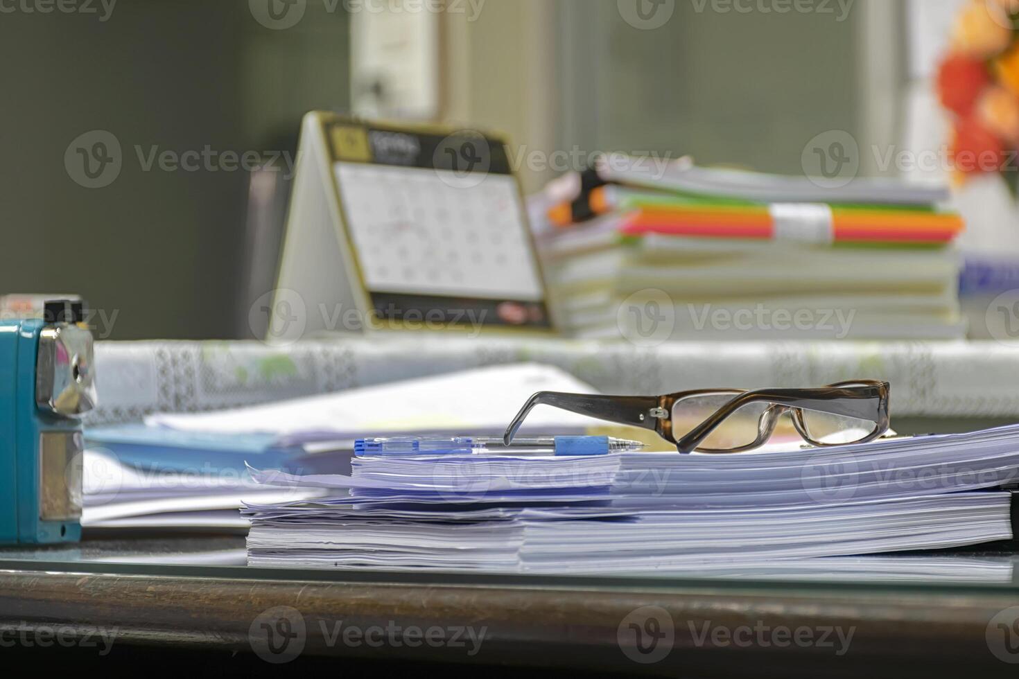 Many documents are placed on the desk.Pen and goggles are placed on it. photo
