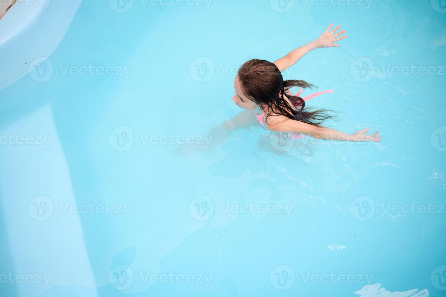 Young girl swimming in a pool, enjoying a summer day with open arms photo