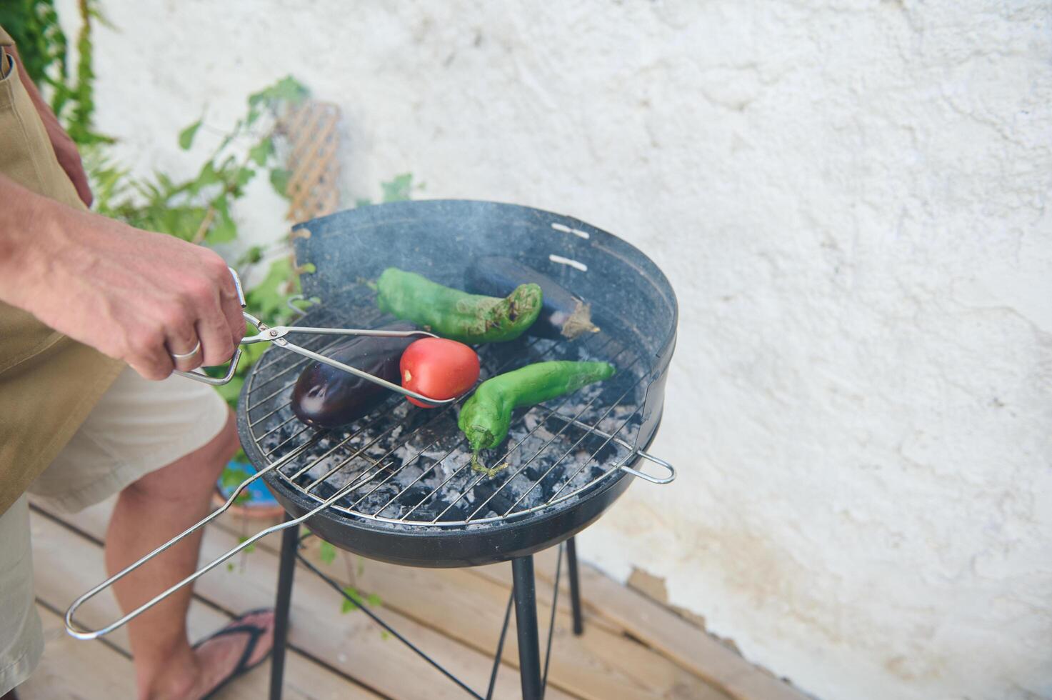 Man grilling fresh vegetables on a barbecue, including tomato, eggplant, and peppers outdoors photo