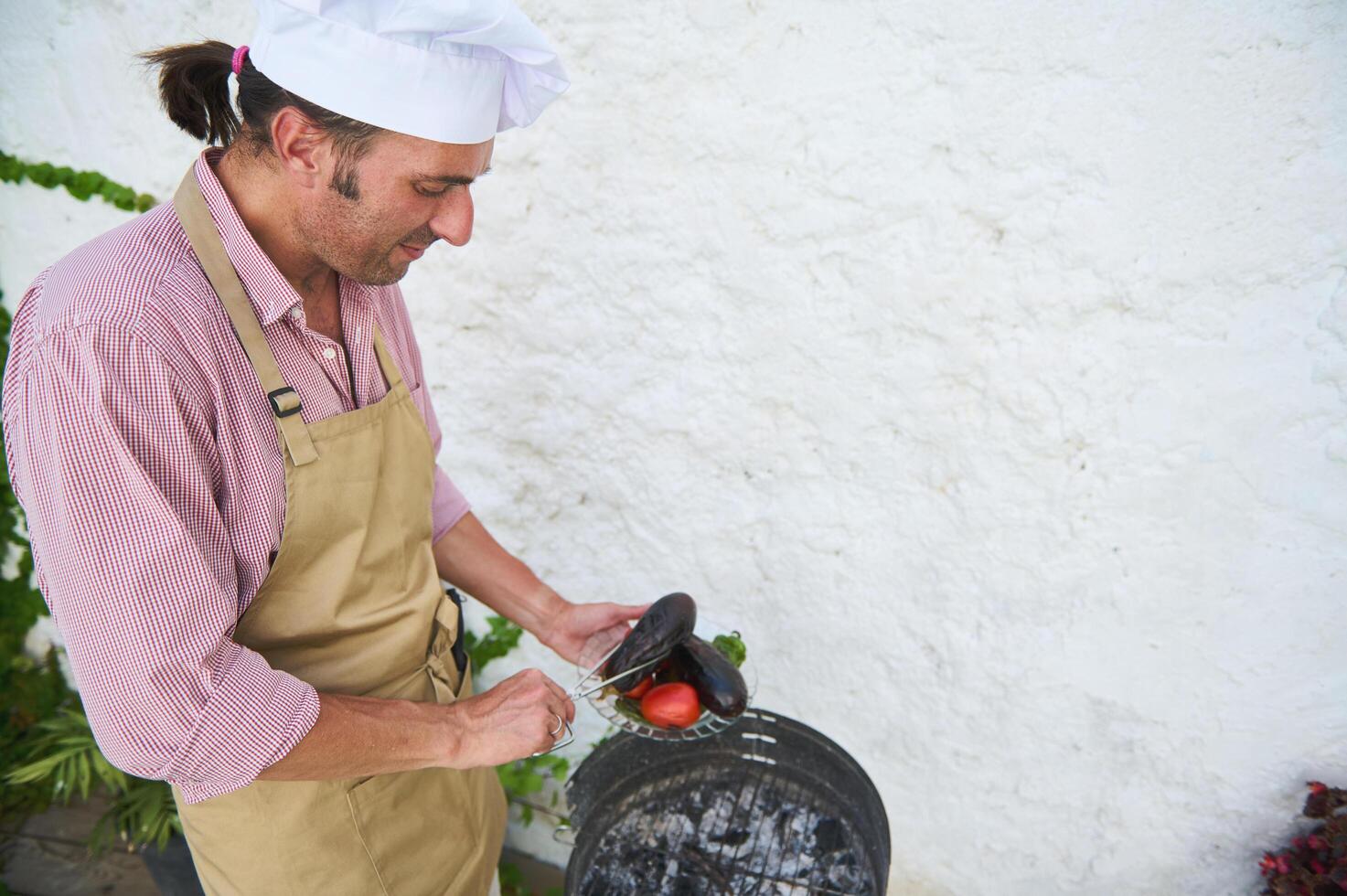 Chef grilling vegetables outdoors in a sunny courtyard, wearing apron and chef hat photo