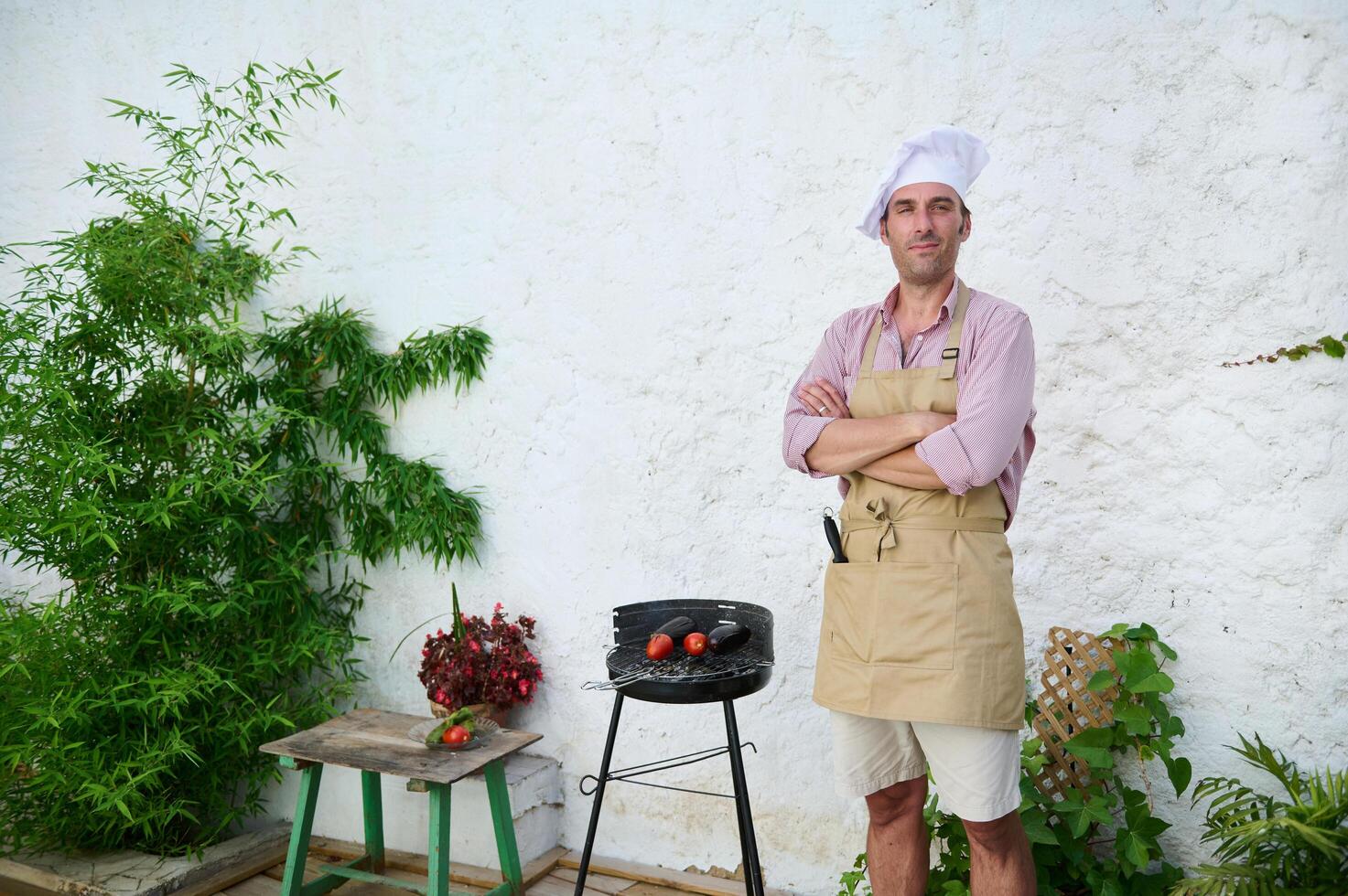 Confident chef standing outdoors near barbecue grill with fresh vegetables photo