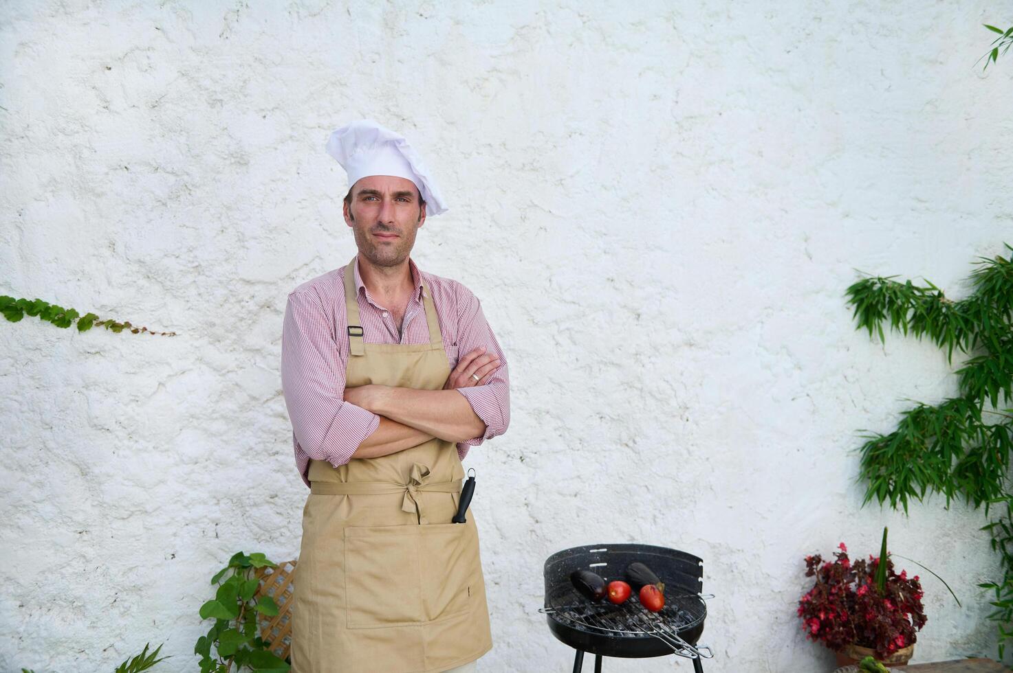 Confident chef in apron and hat standing beside a grill with vegetables photo