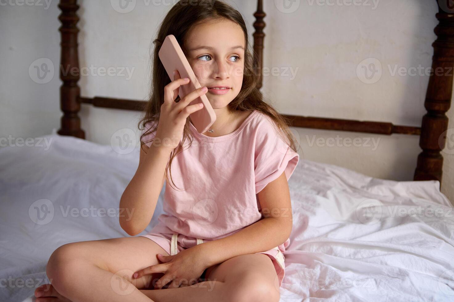 Young girl talking on phone while sitting in bed, smiling dreamily looking away photo