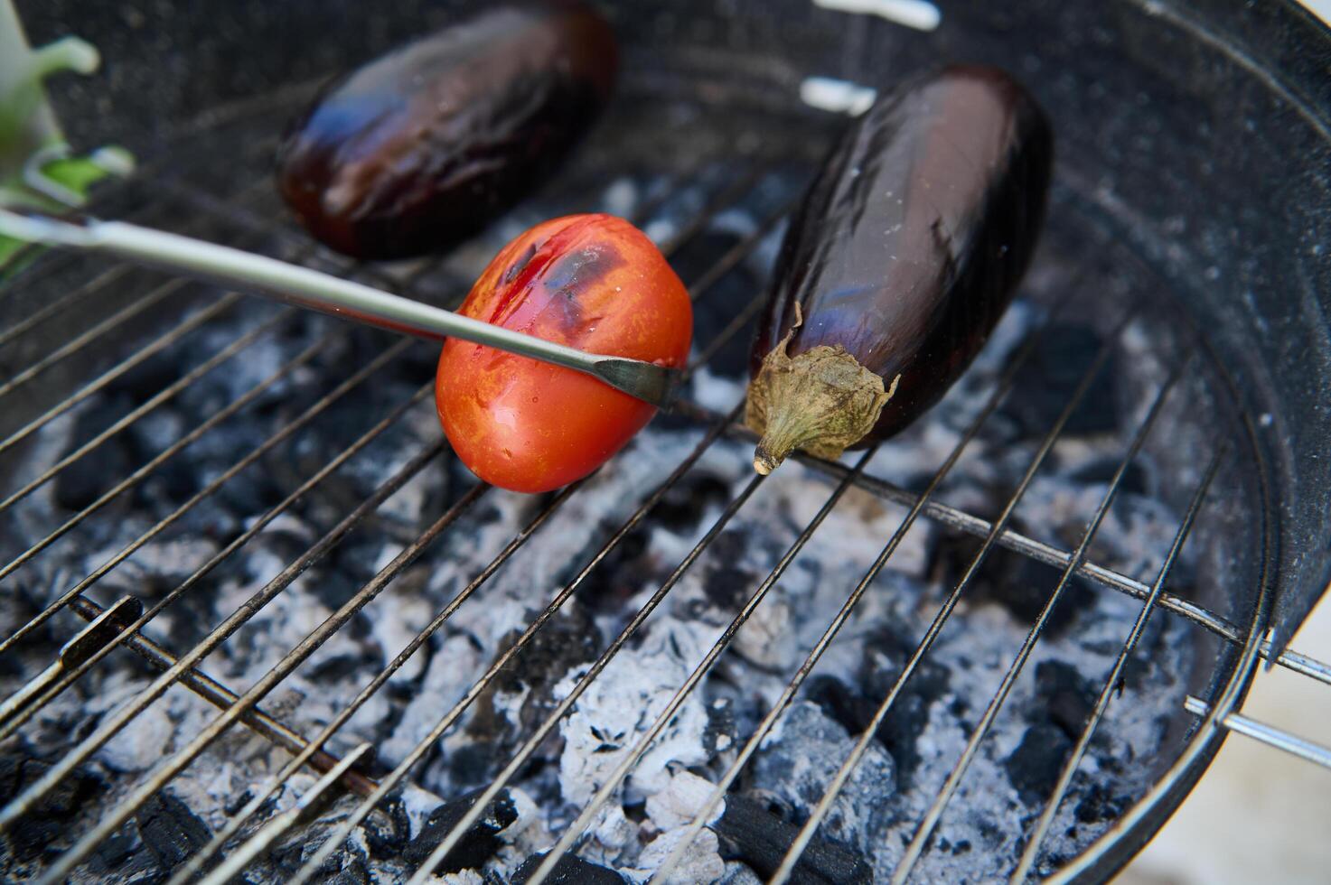 Grilling fresh vegetables on a charcoal barbecue including eggplants and tomatoes photo