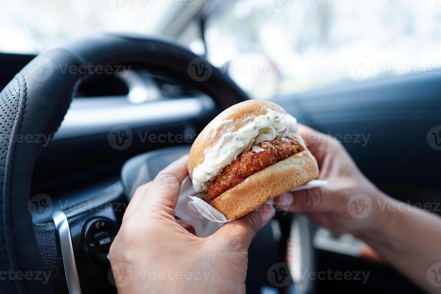 Asian woman driver hold and eat hamburger in car, dangerous and risk an accident. photo