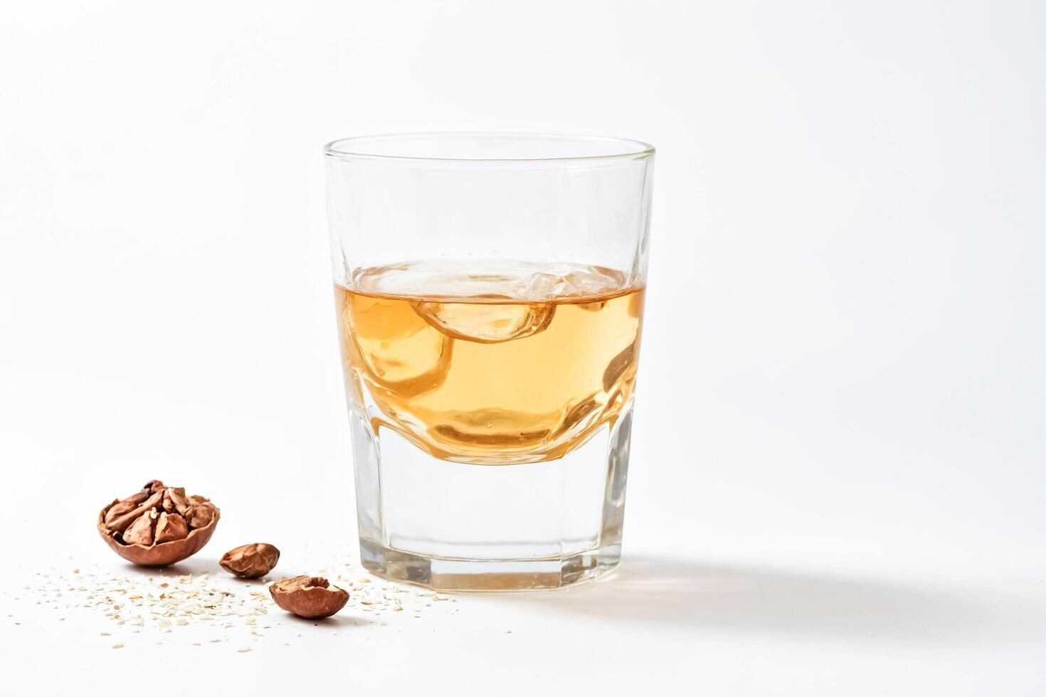 Glass of golden liquid with walnut shells on white background photo