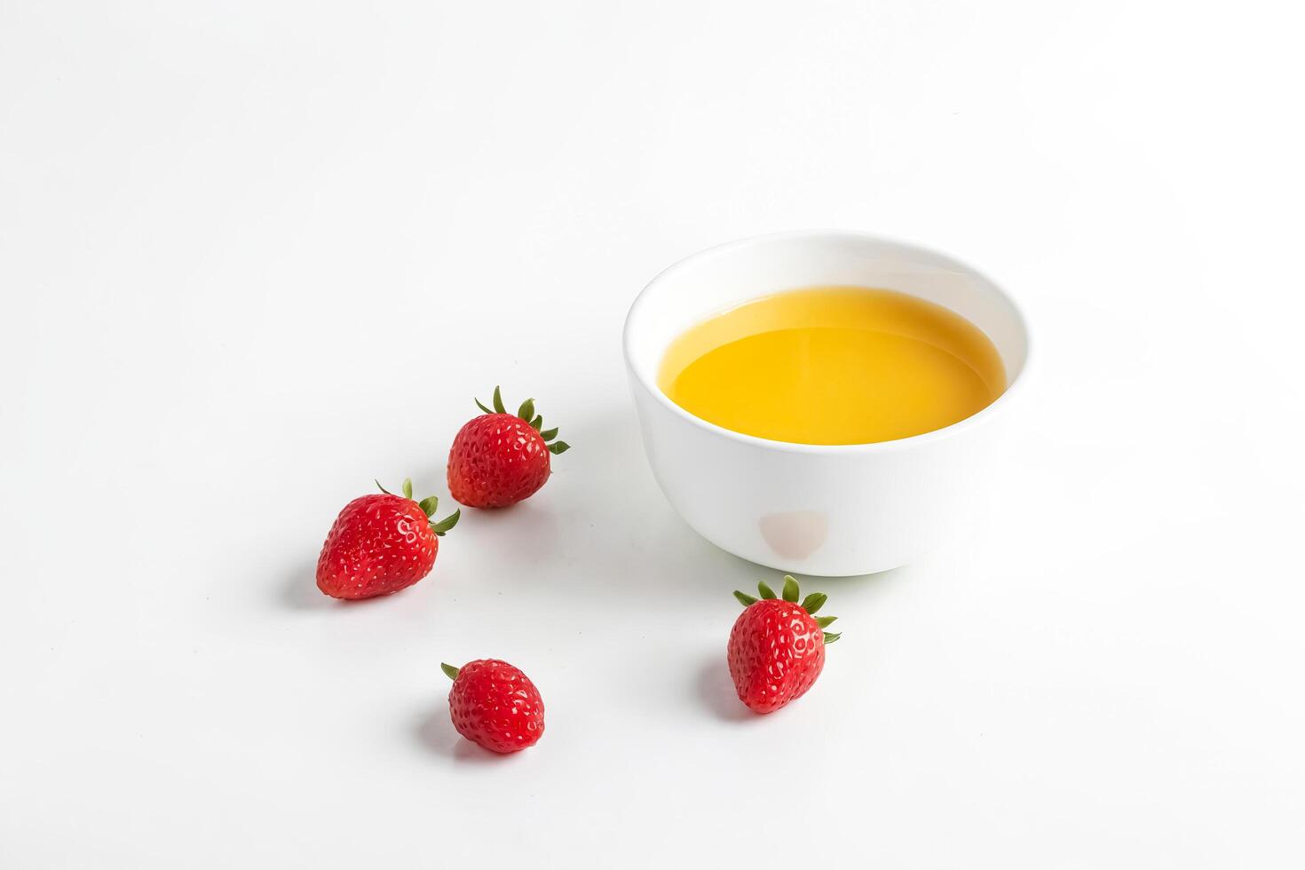 Close-up of a white bowl of yellow liquid and strawberries on a white background photo