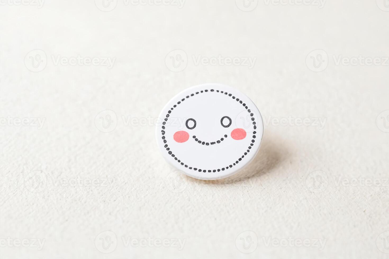White Smiley Face Button with Black Outline and Pink Cheeks on a White Surface photo