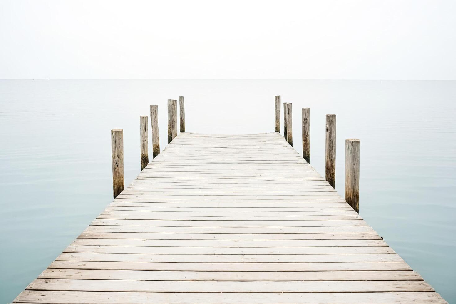 Wooden pier leading out to calm sea with white sky photo