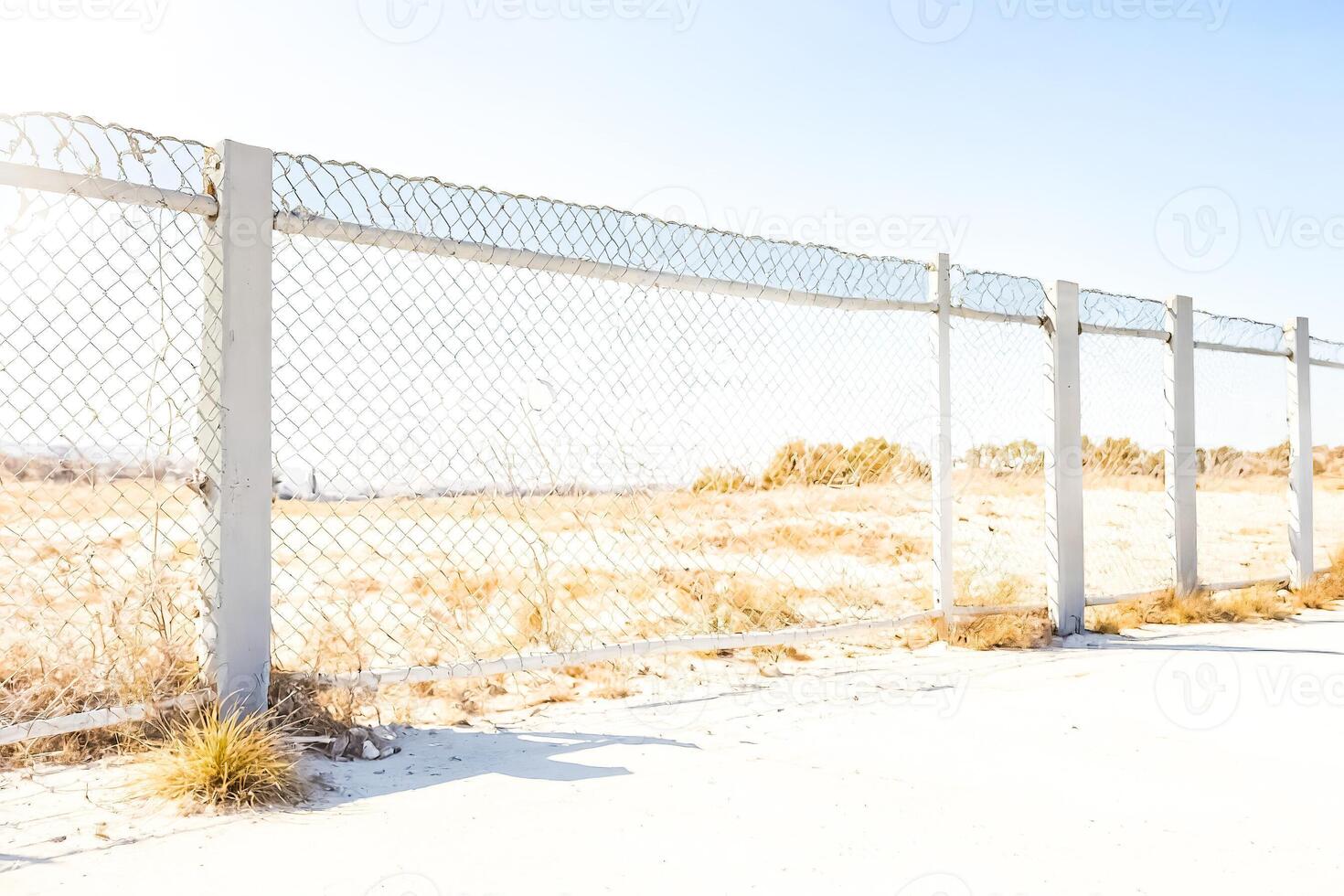 Chain Link Fence with White Posts in Front of Dry Grass Field photo