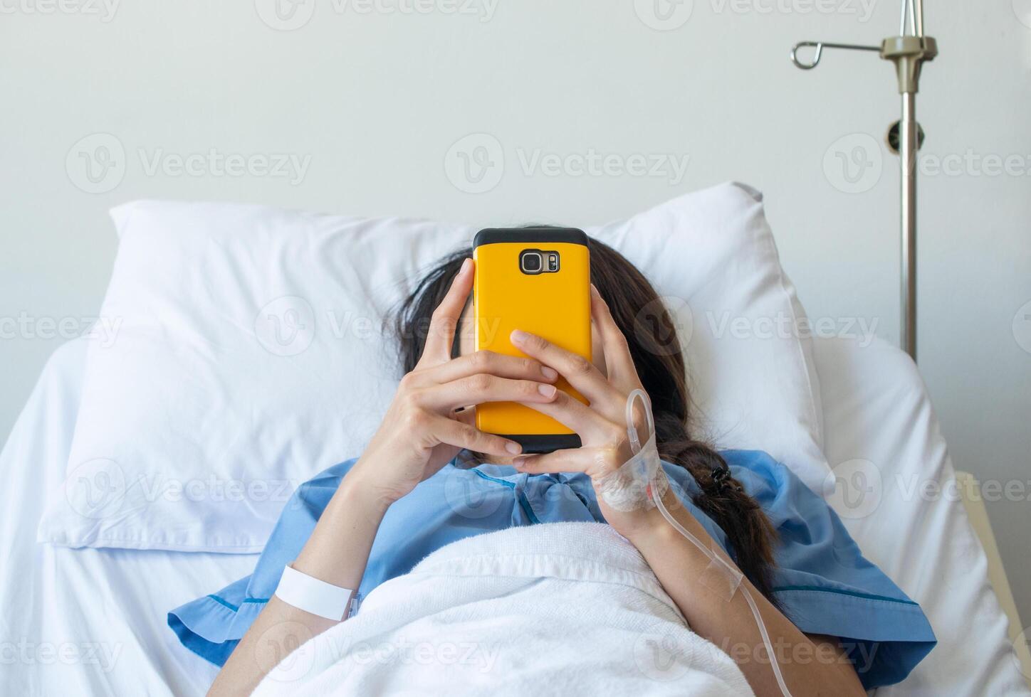 Patient woman lying on bed in hospital and receiving intravenous fluid directly into a vein but she still playing her social network on smartphone. photo
