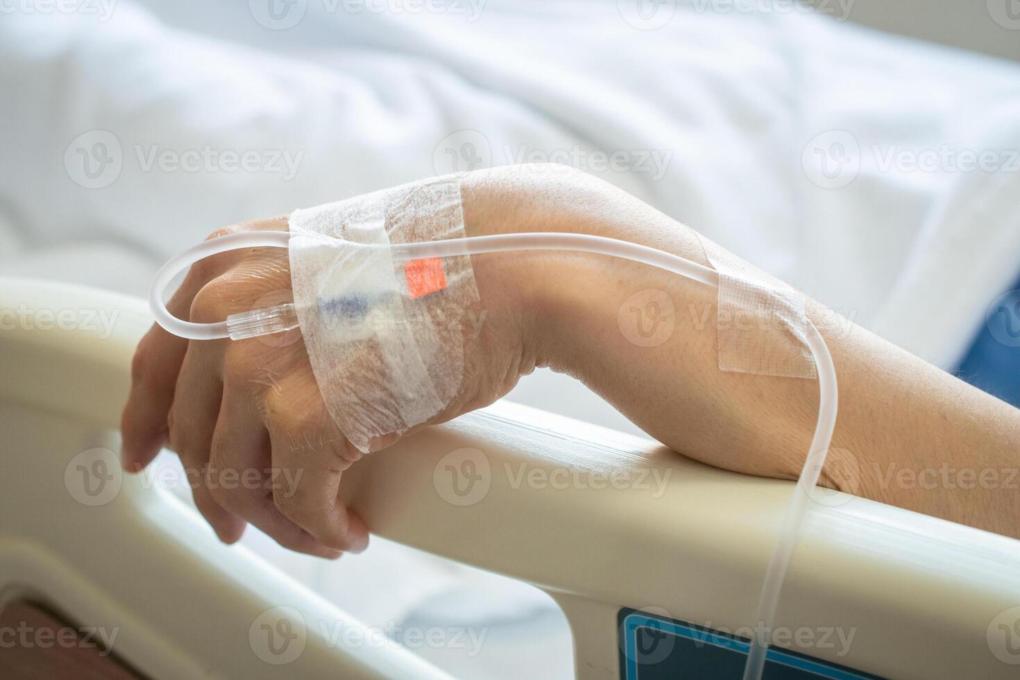Close up of patient woman hand with receiving intravenous fluid directly into a vein while her hand touching bed rails on hospital bed. Conceptual of patient woman resting in hospital. photo