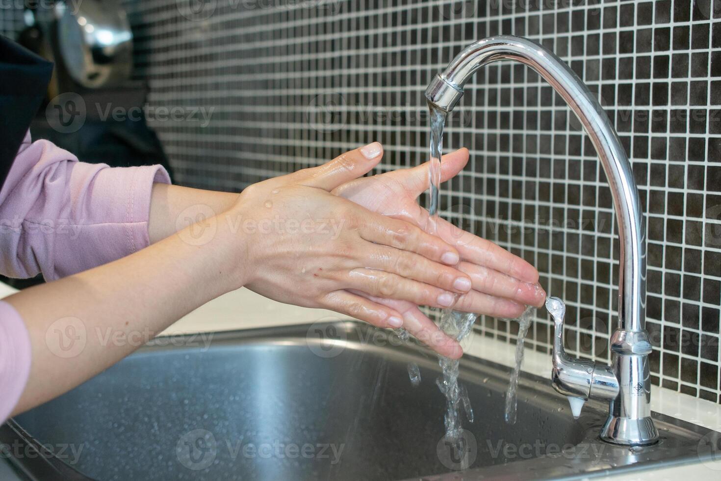 Cropped shot view of woman washing hands at sink basin faucet in kitchen room. Washing your hands is one of the easiest ways to protect yourself and others from illnesses. photo