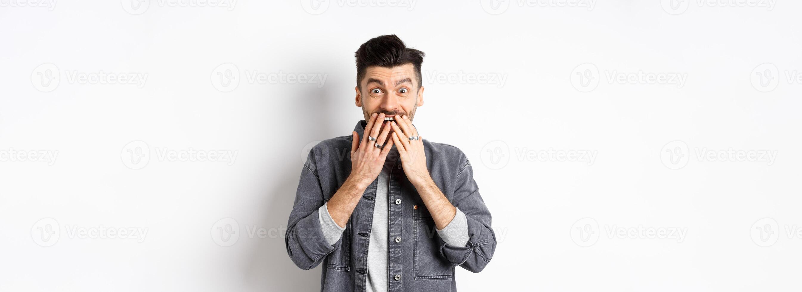 Excited happy man laughing from happiness, look with surprise and disbelief, receive gift, standing on white background photo