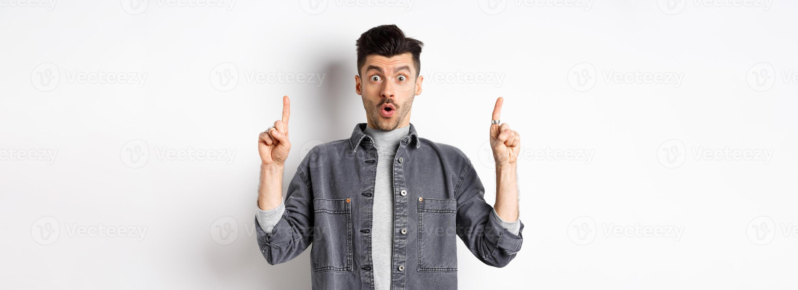 Excited man checking out promo offer, gasping amazed and pointing fingers up, making cool announcement, standing on white background photo