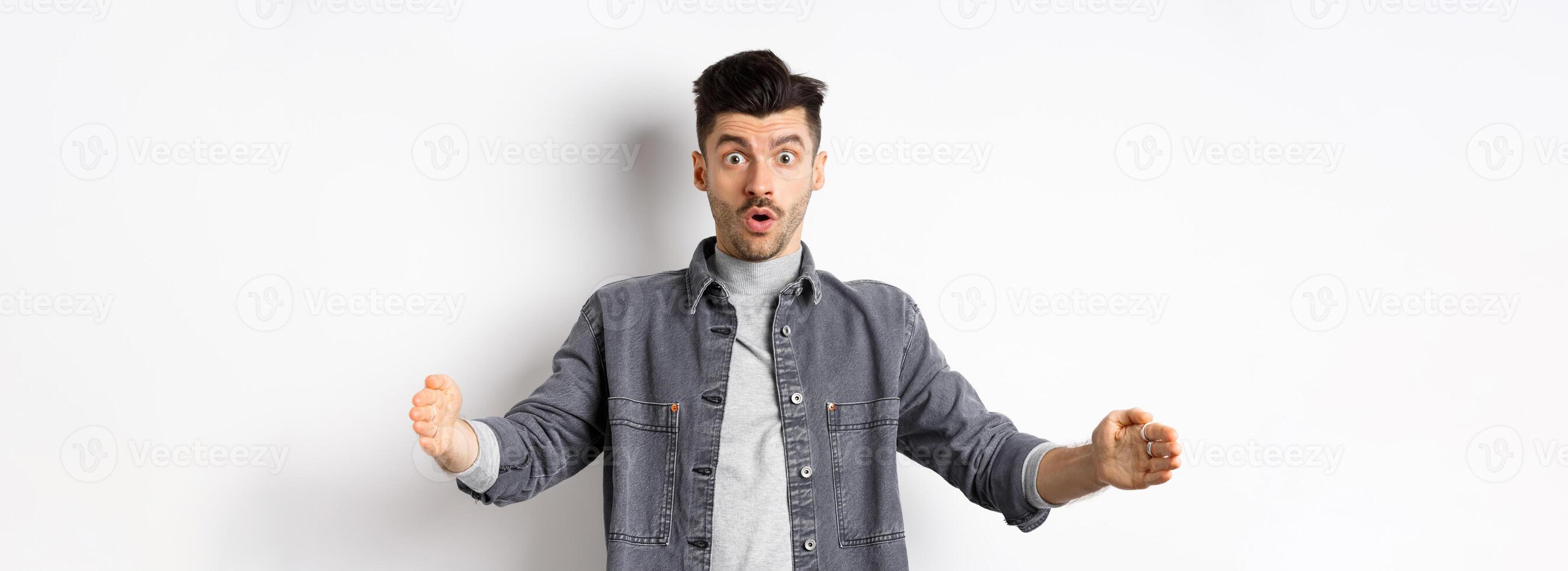 Excited caucasian man showing big size, shaping large object and look amazed, standing on white background photo