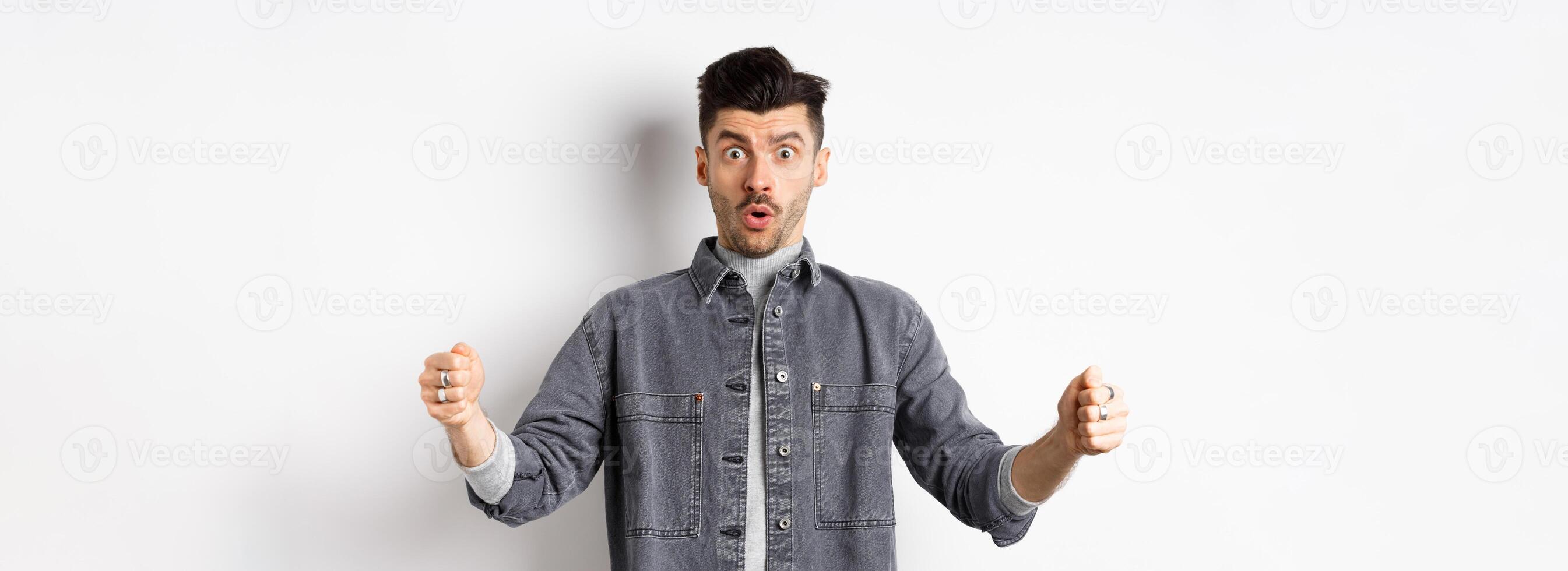 Confused man holding big size object and looking shocked, shaping large thing, standing on white background photo
