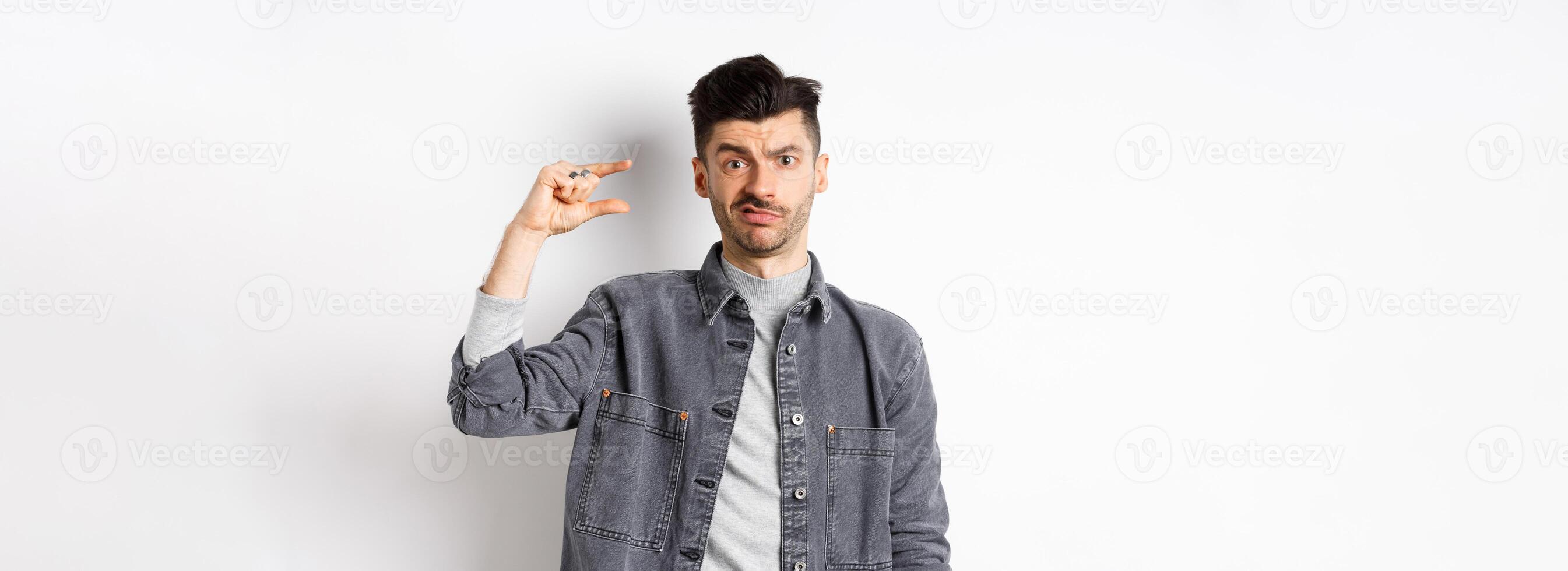 Disappointed guy showing small size and grimacing upset, frowning displeased with little thing, standing on white background photo