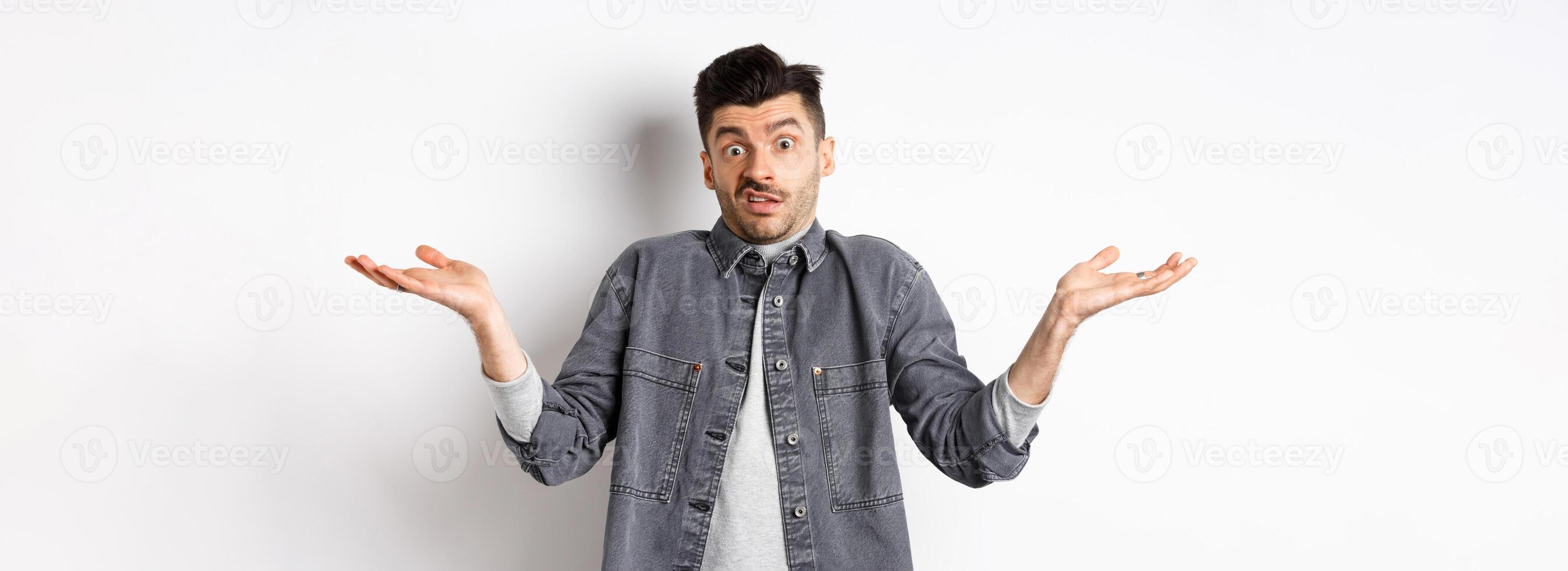 I dont know. Clueless young man shrugging and looking confused, have nothing to say, standing unaware on white background photo