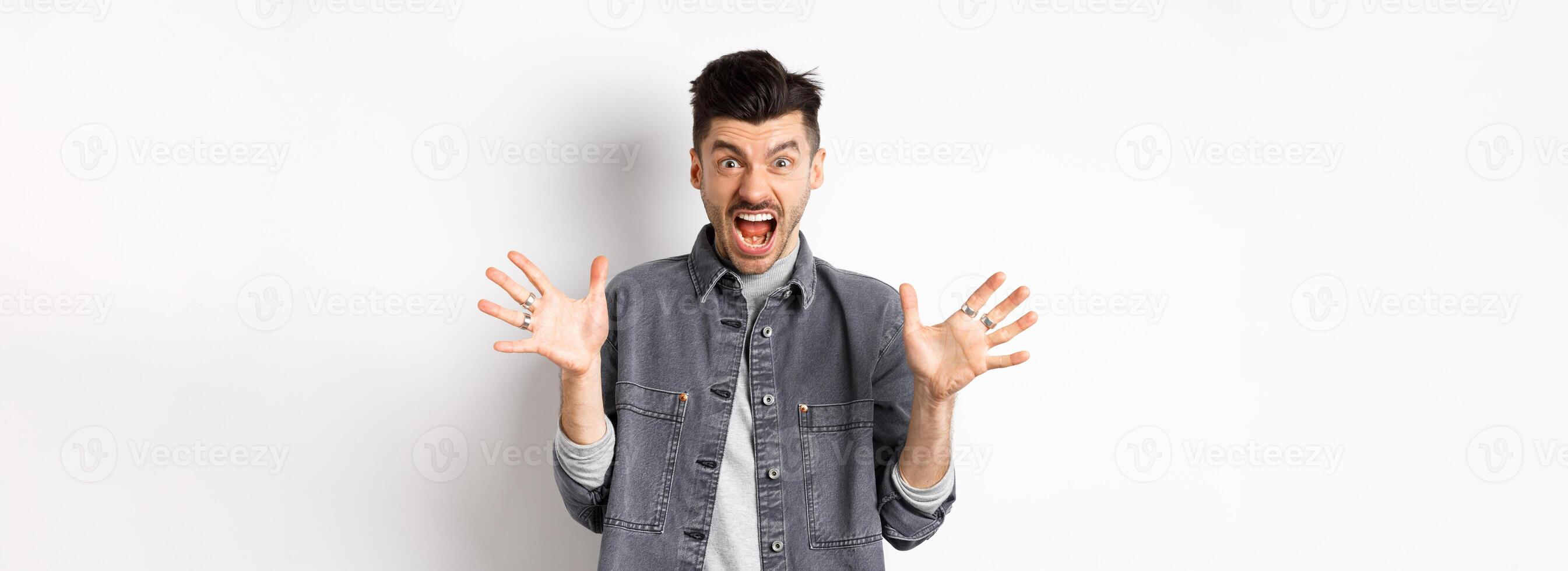 Angry man scream and look scary at camera, shouting with furious and hateful expression, standing on white background photo