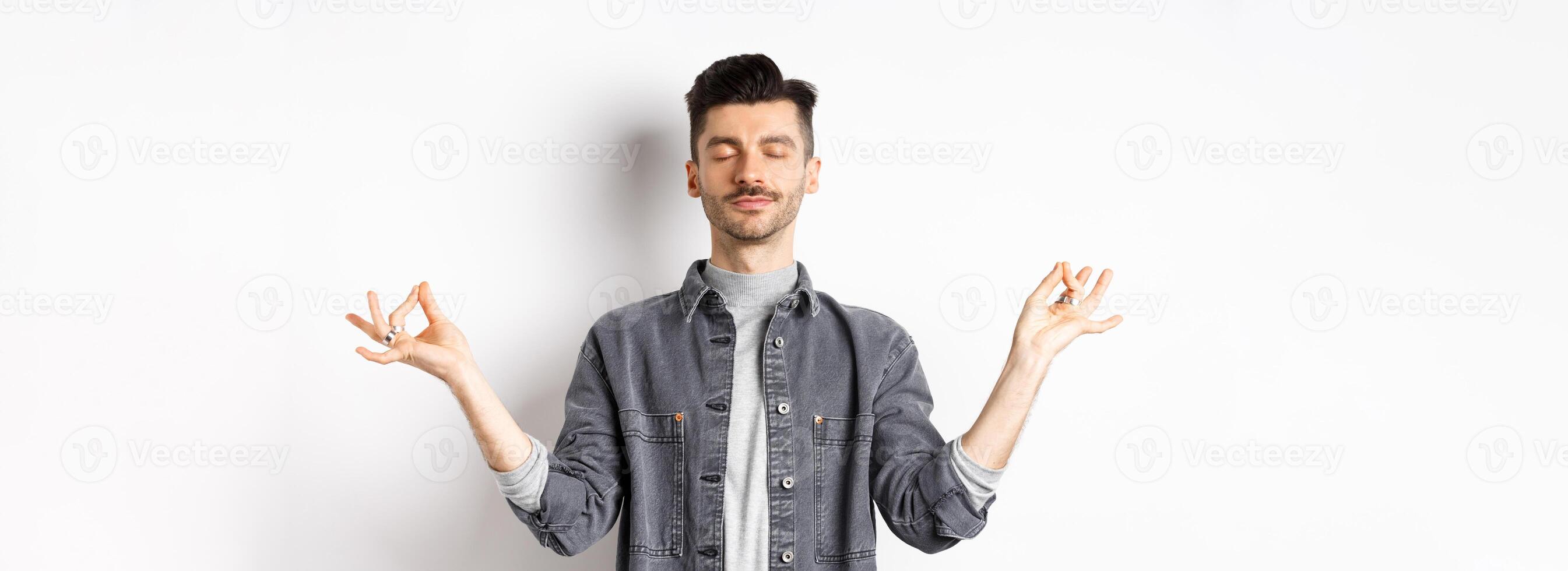 Calm guy meditating with peaceful face, holding hands in zen mudra sign and close eyes, practice yoga, relaxing on white background photo