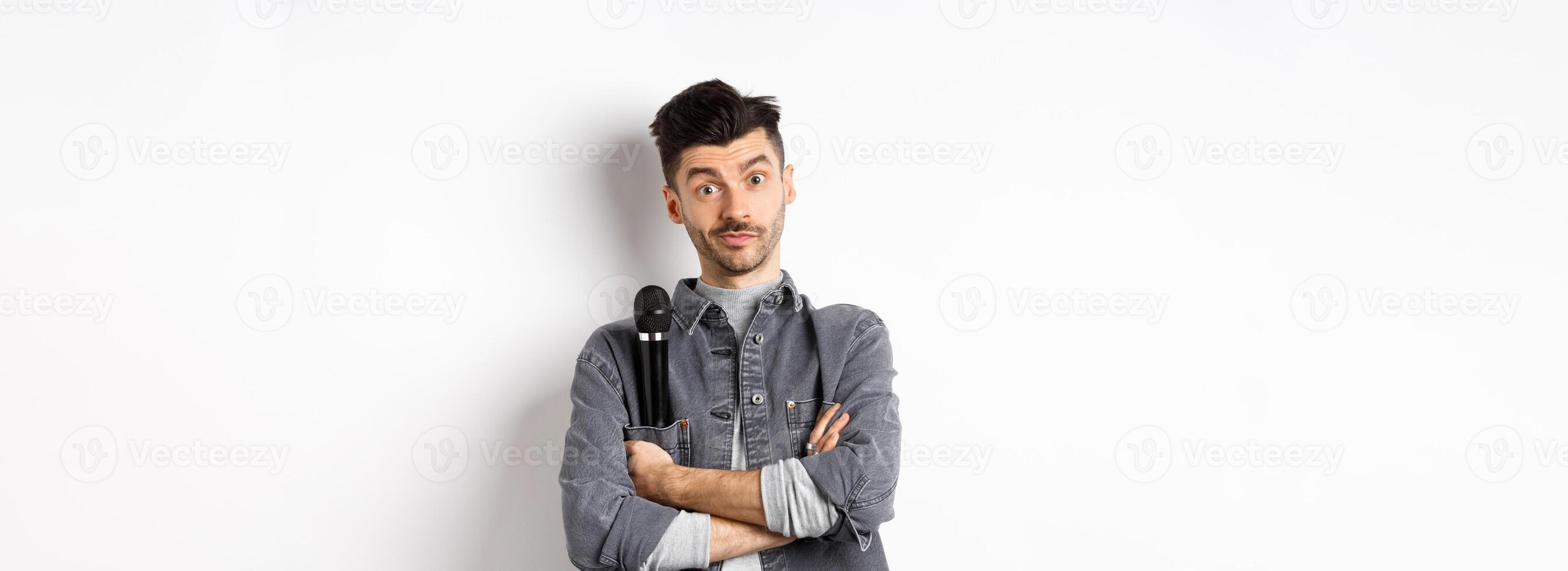 Image of funny male entertainer or singer, holding microphone in pocket of jacket and look at camera with arms crossed, standing against white background photo