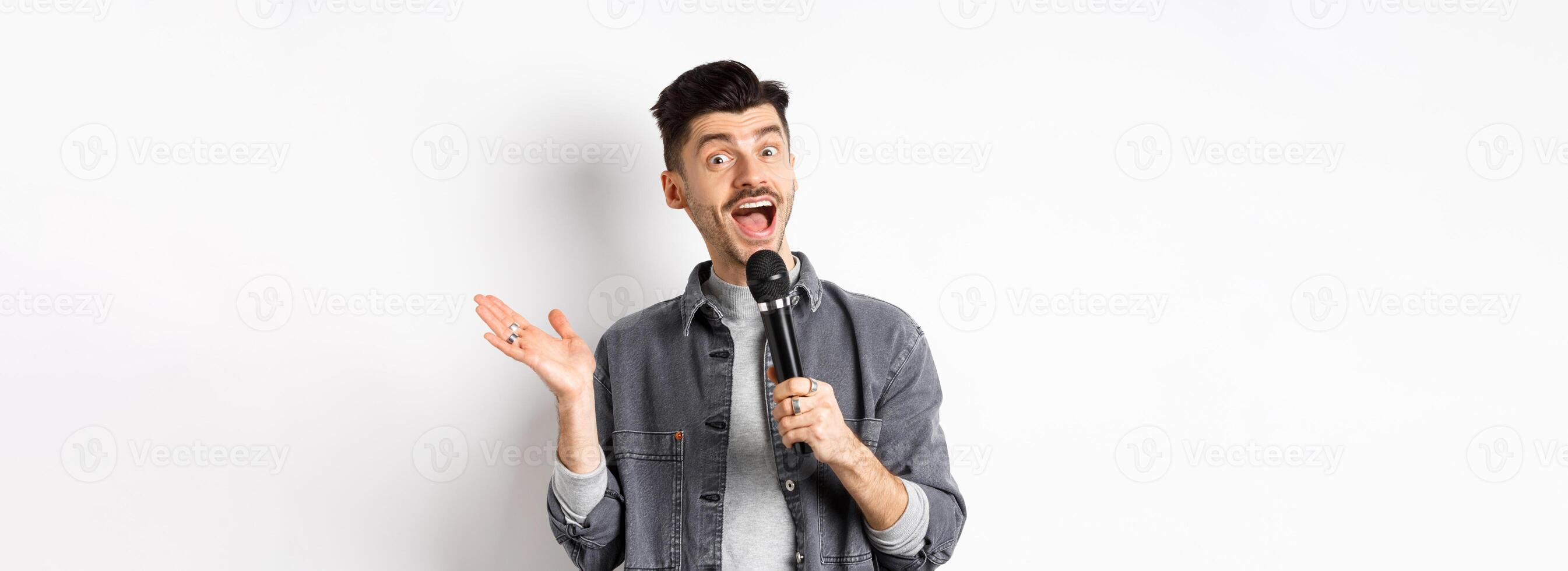 Excited stylish guy giving speech, talking in microphone, perform or sing karaoke, standing on white background photo