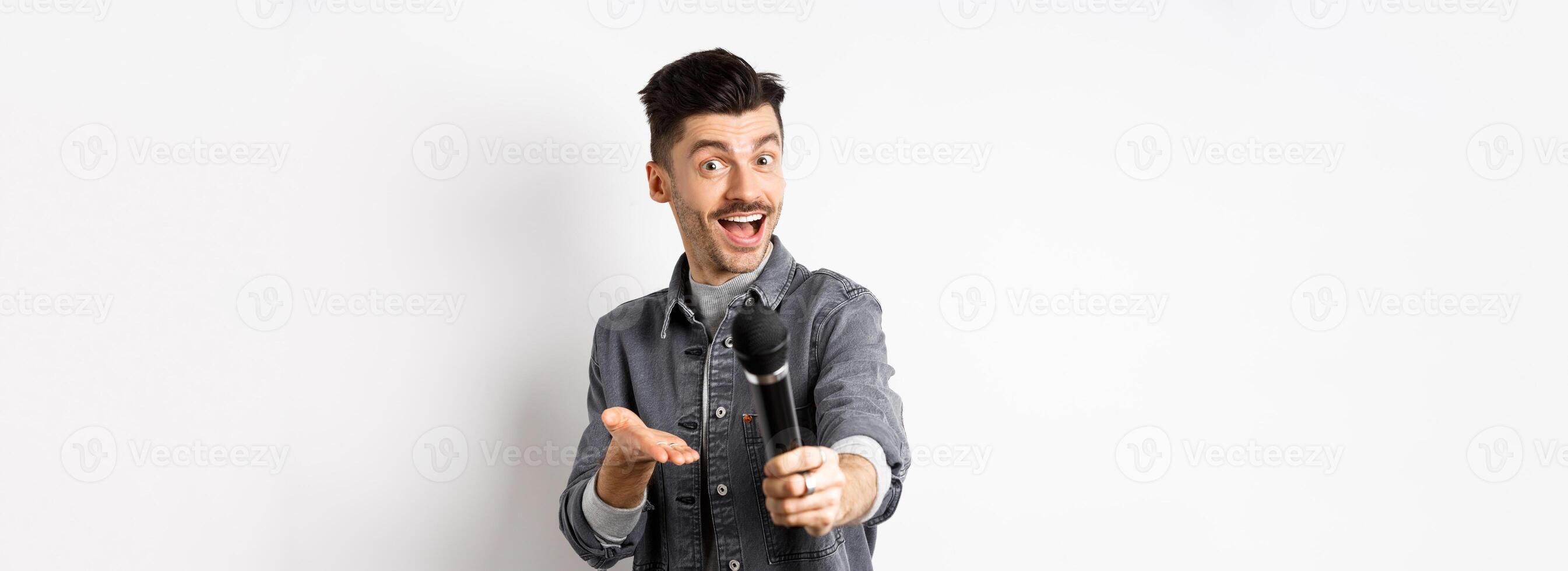 Handsome smiling man stretch out hand with microphone, giving you mic, standing on white background photo