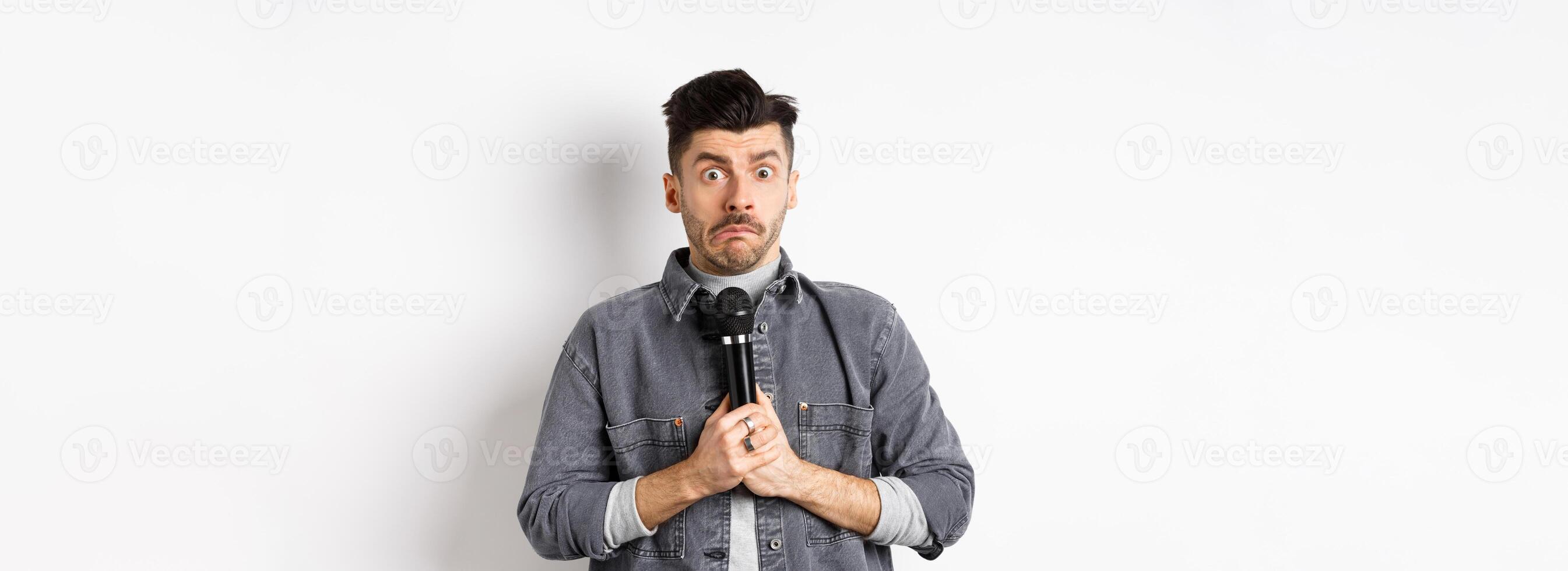 Nervous unconfident guy holding microphone and look indecisive, scared to perform, standing shy against white background photo