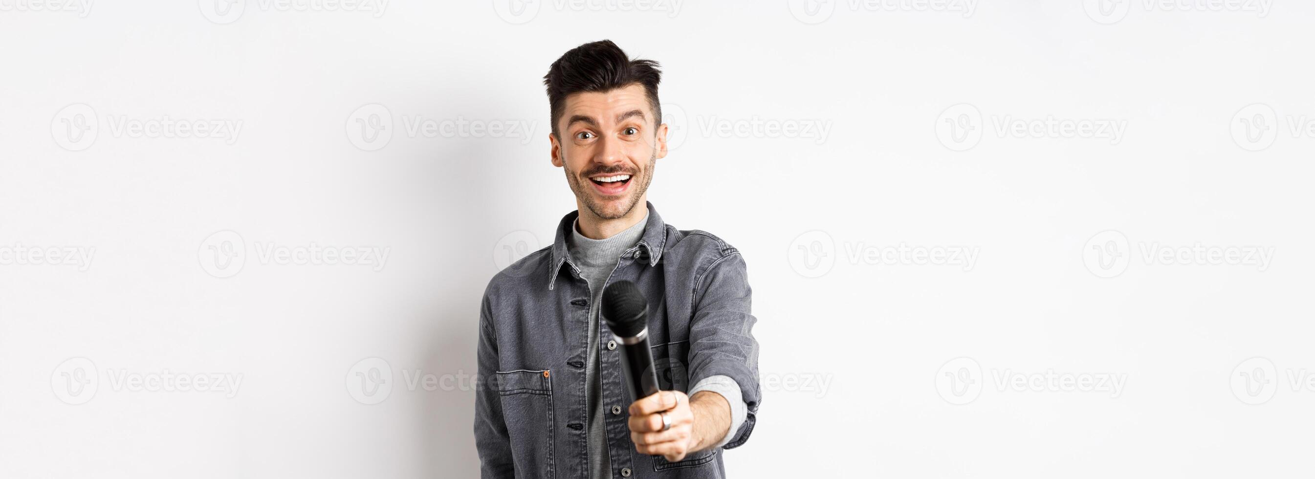 Handsome smiling man stretch out hand with microphone, giving you mic, standing on white background photo