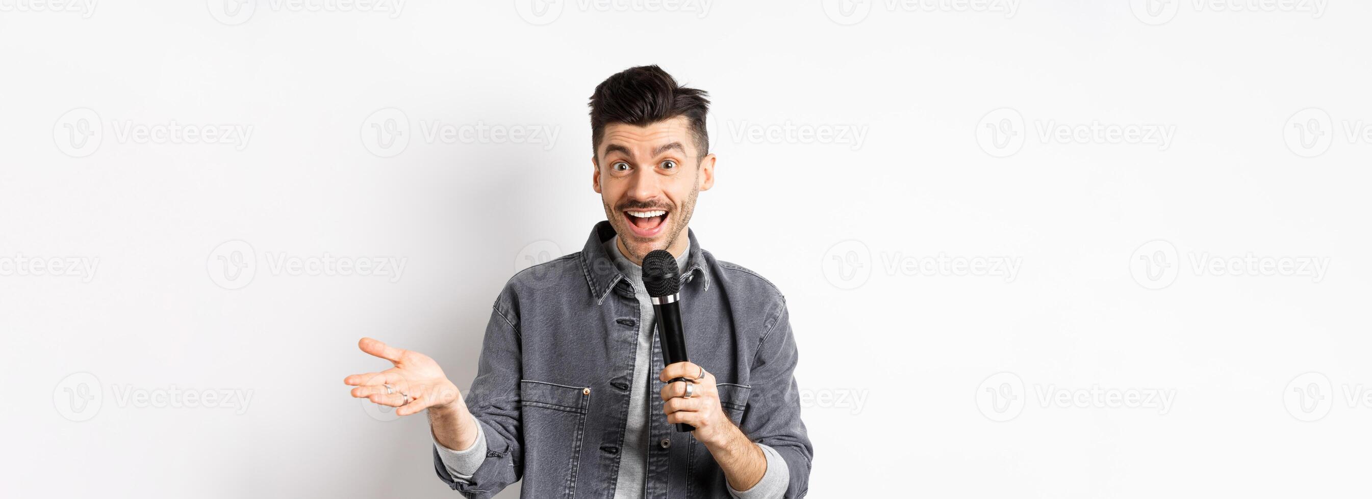 Handsome smiling performer talking in mic, gesturing and performing, making speech with microphone, standing against white background photo