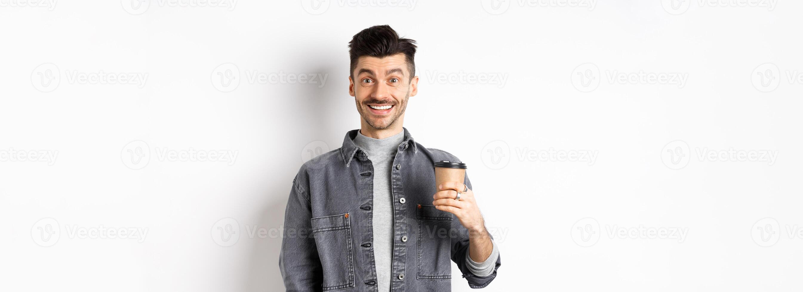 Enthusiastic handsome man holding coffee cup and smiling, drinking good drink from cafe takeout, standing against white background photo