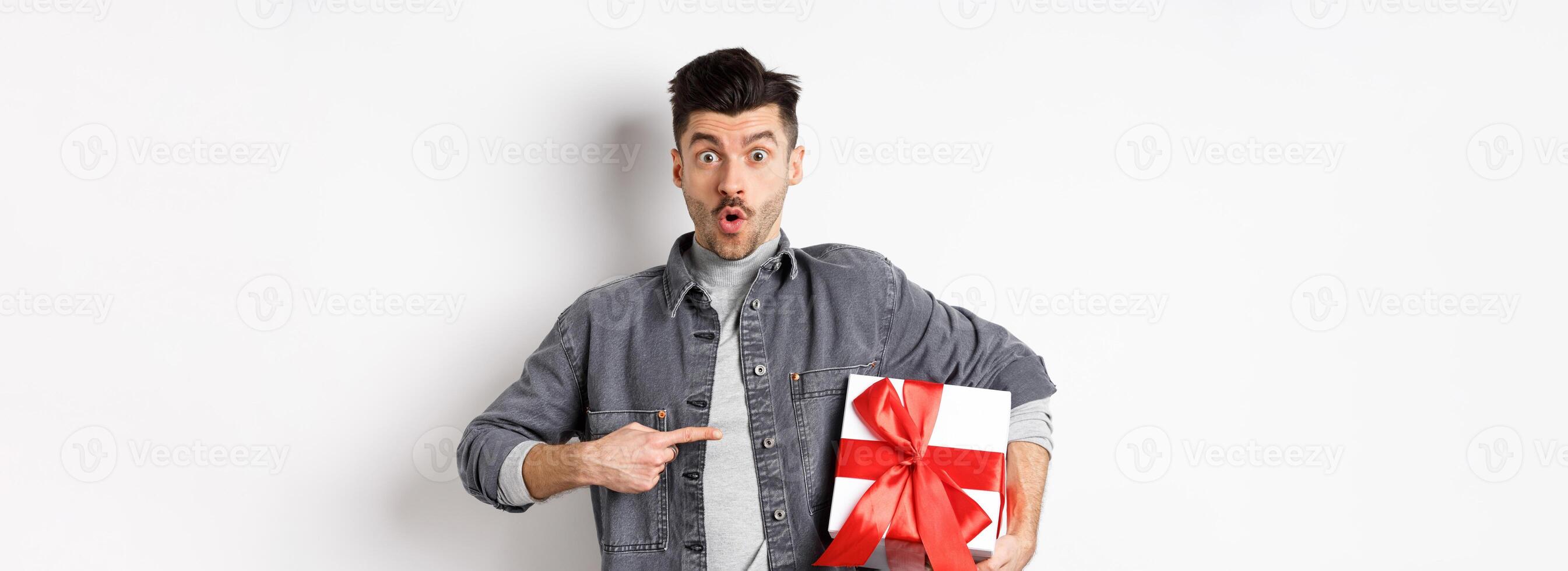 Happy Valentines day. Man shopping for romantic date, pointing at gift box and looking amazed, saying wow impressed, showing lover present, white background photo