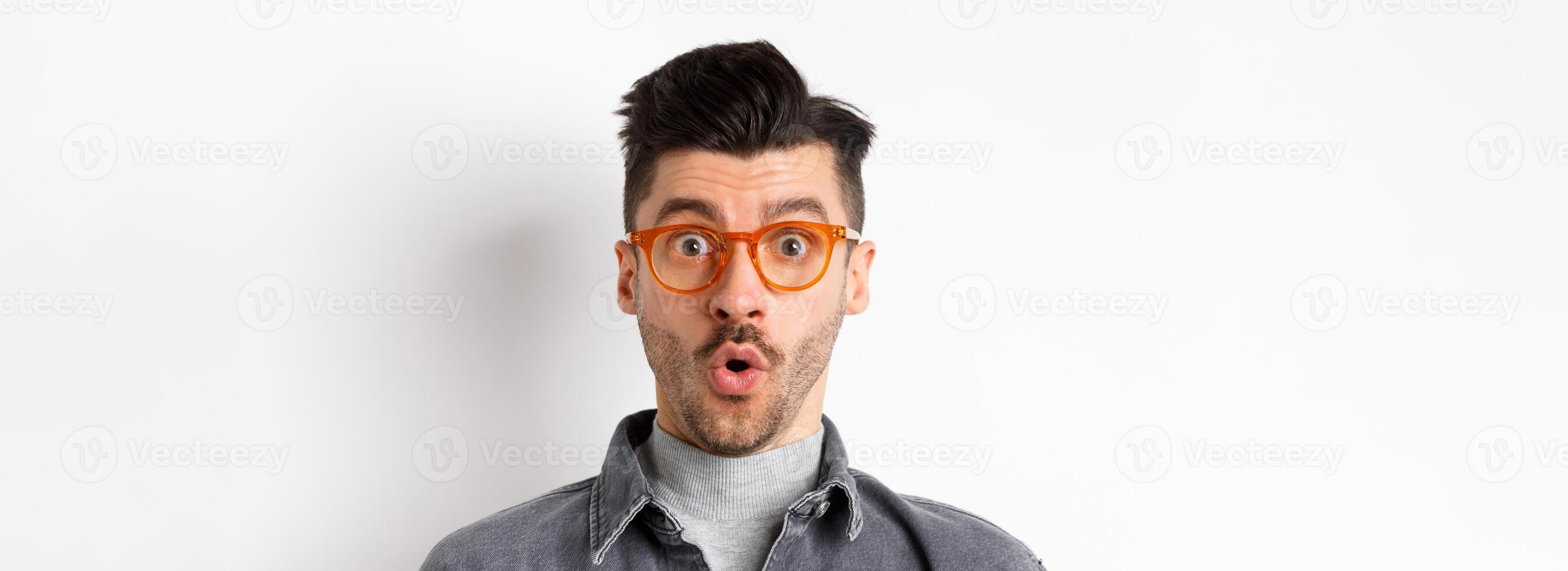 Wow look there. Excited handsome man in stylish glasses stare impressed at camera, checking out eyewear store offer, standing on white background photo