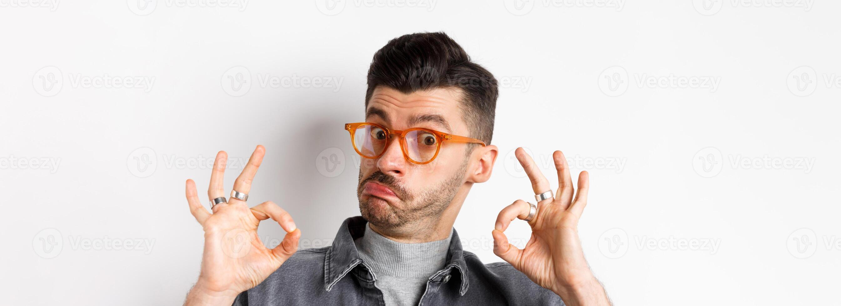 Not bad. Impressed man in stylish glasses showing okay signs and nod in approval, prase good thing, making compliment, standing on white background photo