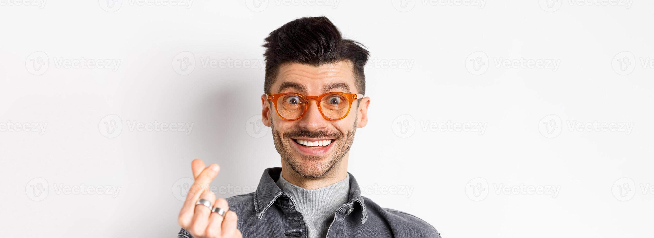 Close up portrait of cute guy with moustache wearing glasses, showing hand heart sign, smiling happy, standing on white background photo