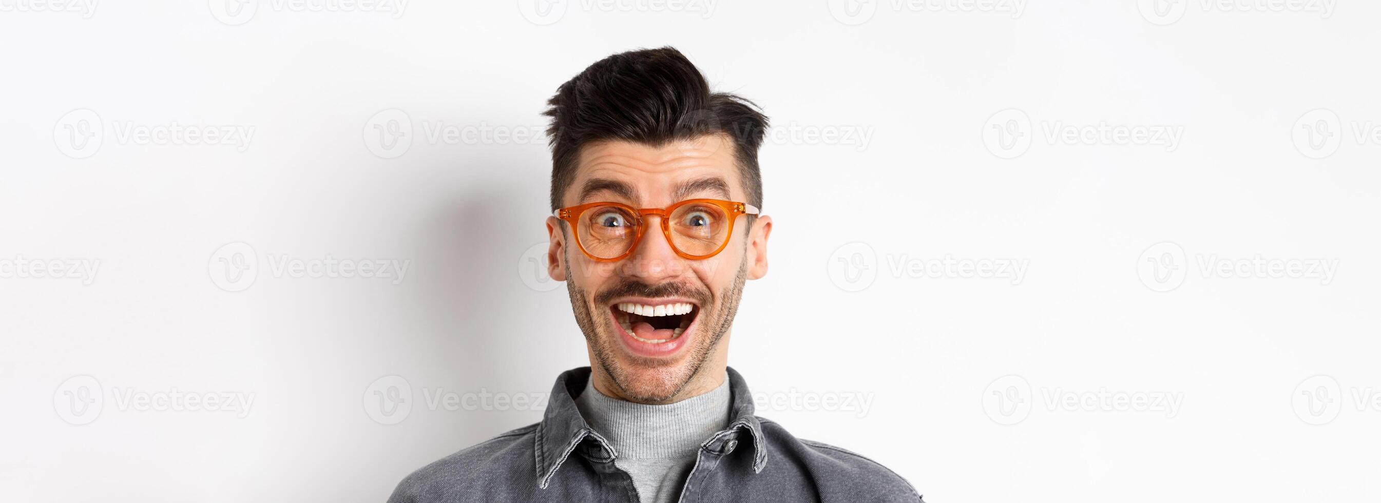 Excited funny man in glasses smiling, look with amazement and joy at awesome promo, standing happy against white background photo
