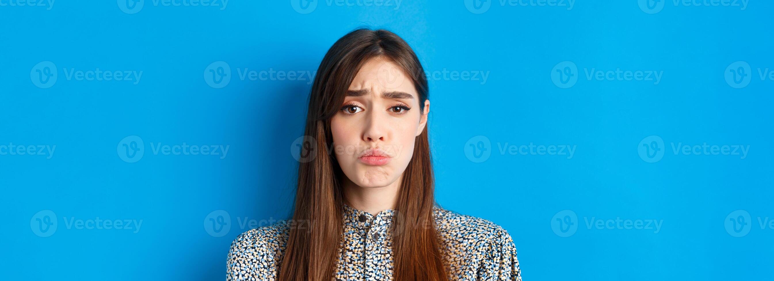 People emotions concept. Sad cute girl begging for something, pucker lips and frowning, whining asking please, standing on blue background photo