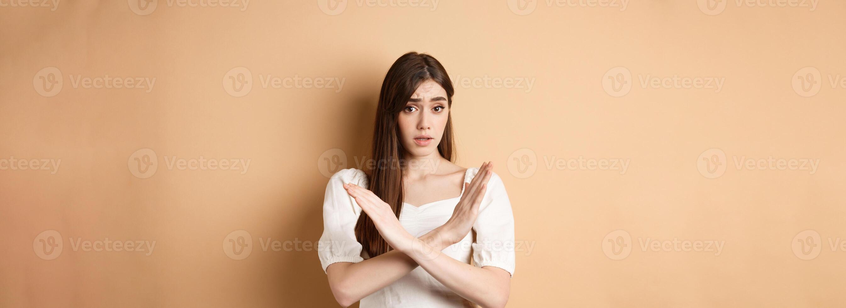 Girl says no. Skeptical young woman disagree or prohibit action, showing cross stop gesture, make nope sign, disapprove bad idea, standing on beige background photo