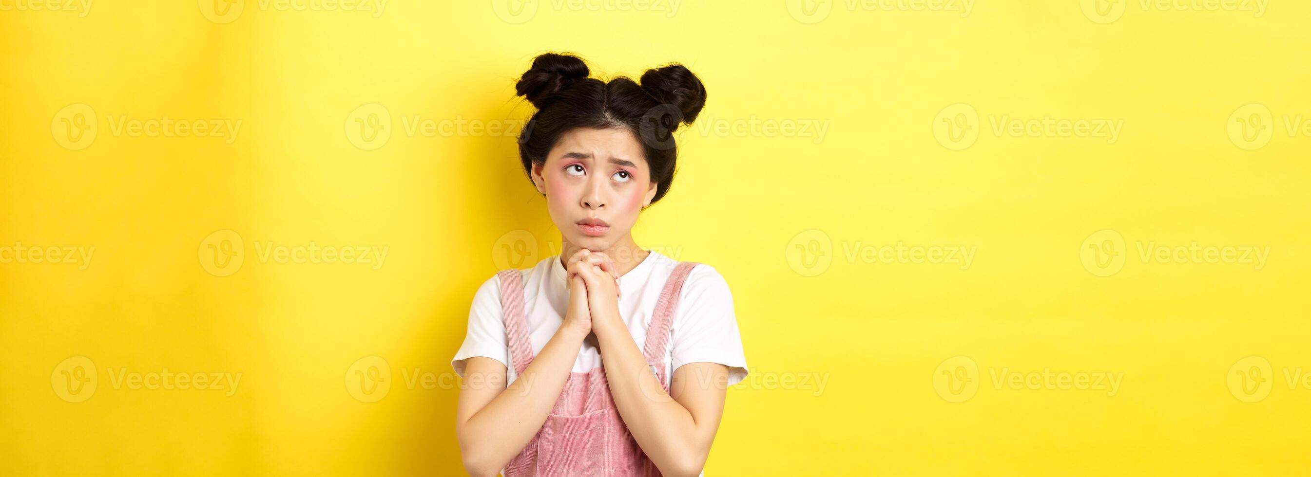 Sas asian girl holding hands in pray, pleading god, looking up and begging, standing on yellow background photo