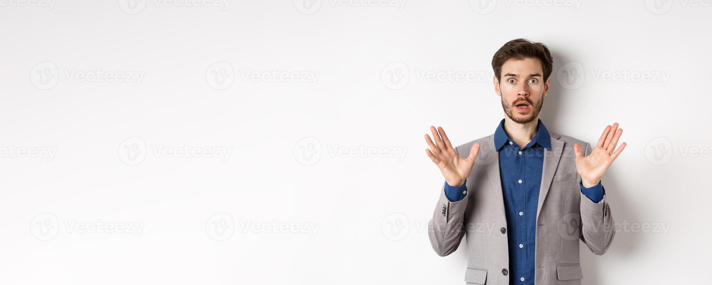 Surprised businessman in suit raising hands up and look excited, standing against white background photo