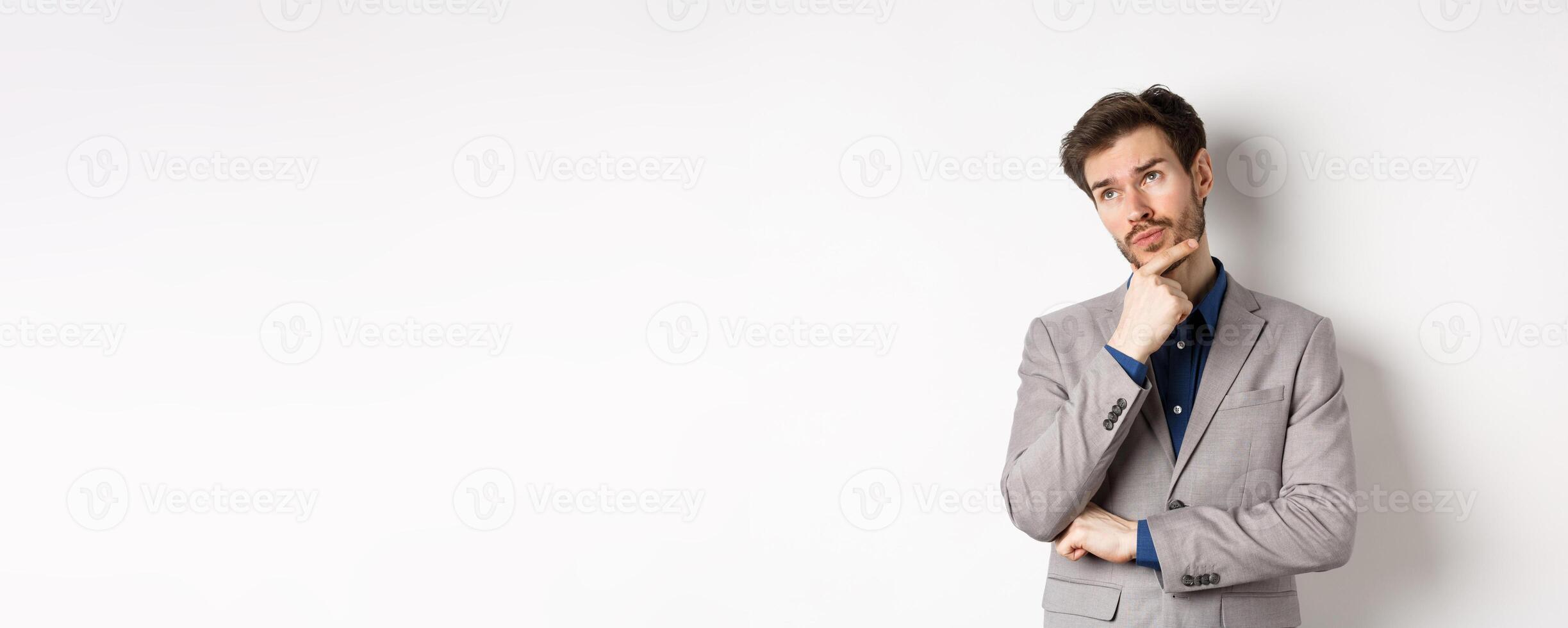 Thoughtful businessman in grey suit look at upper left corner logo, thinking or making choice, pondering plan, standing against white background photo
