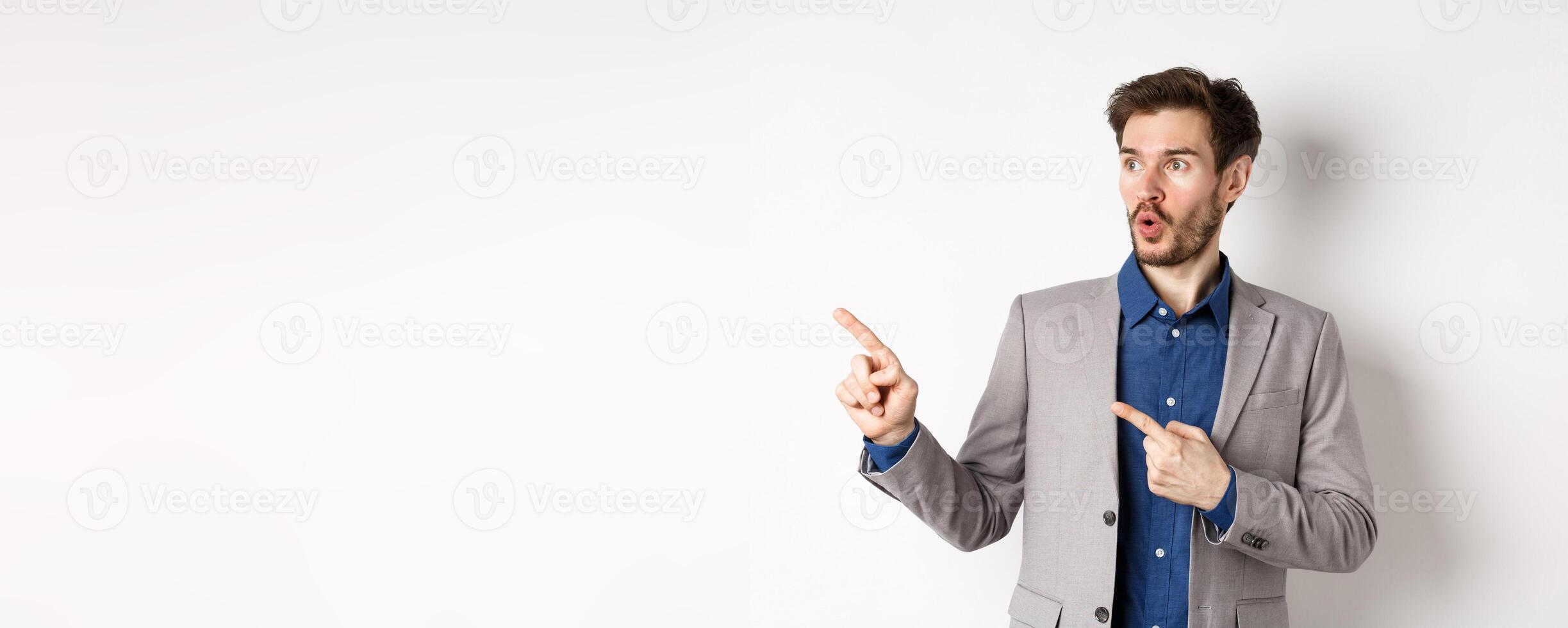 Wow look there. Excited male ceo manage in suit pointing fingers left, looking at logo impressed, showing advertisement, standing on white background photo